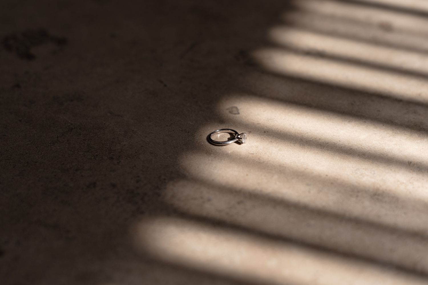 Wedding rings casting shadows through window light on textured surface.