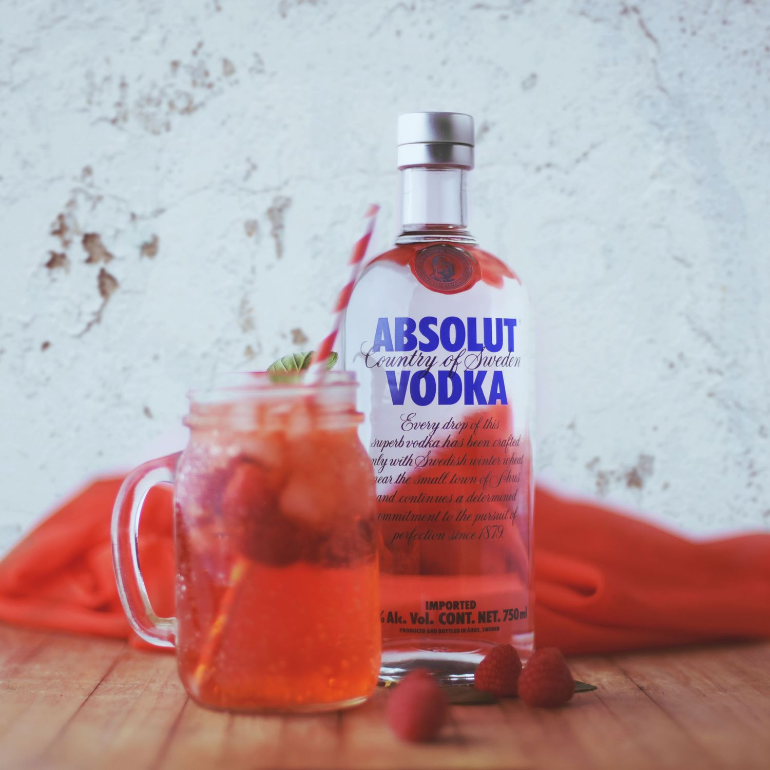 Absolut vodka bottle with red cocktail served in glass on wooden surface.