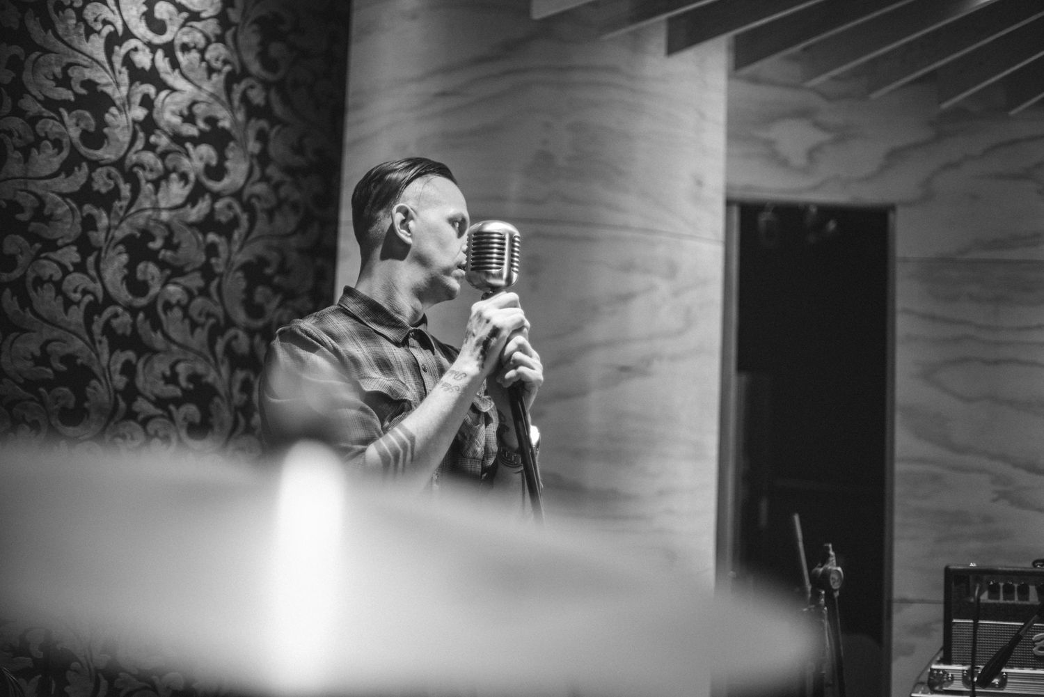 Black and white image of performer singing passionately into microphone on stage with dramatic lighting.