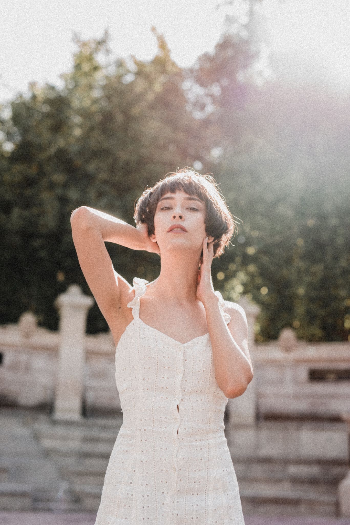 Woman in white sundress poses with closed eyes in warm summer sunlight.