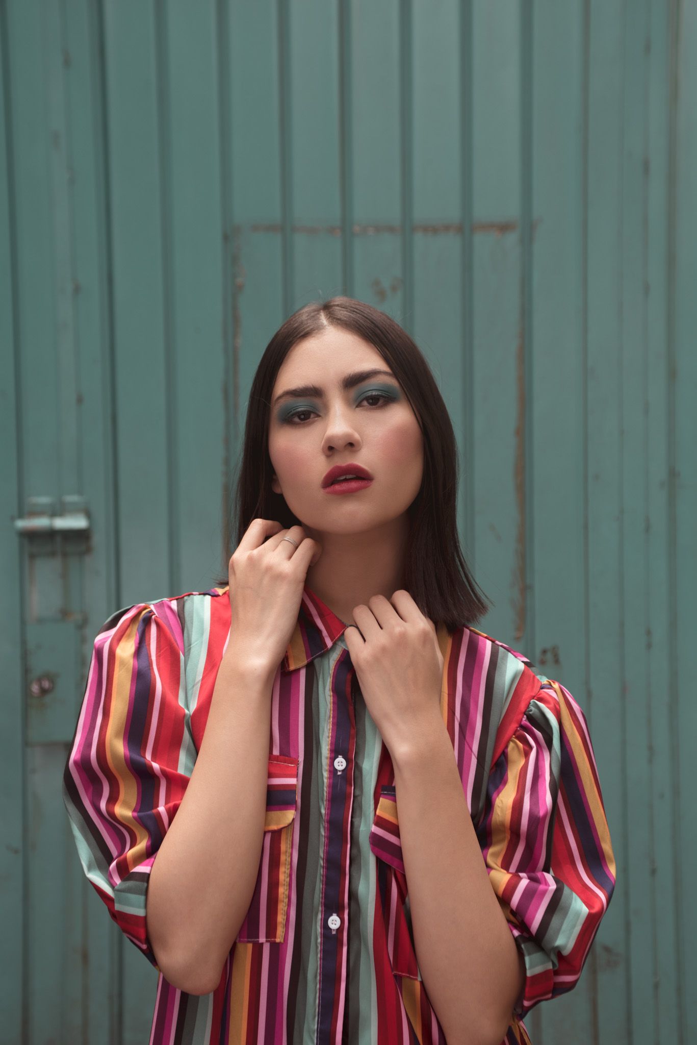 Fashion portrait against teal wall wearing colorful striped button-up shirt.