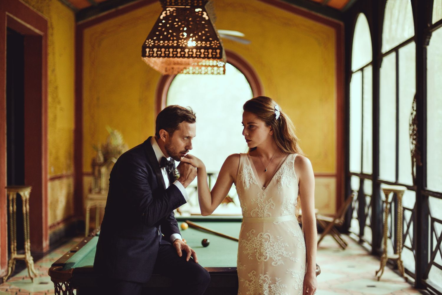 A couple shares a romantic moment in an elegant venue with arched windows and warm lighting.