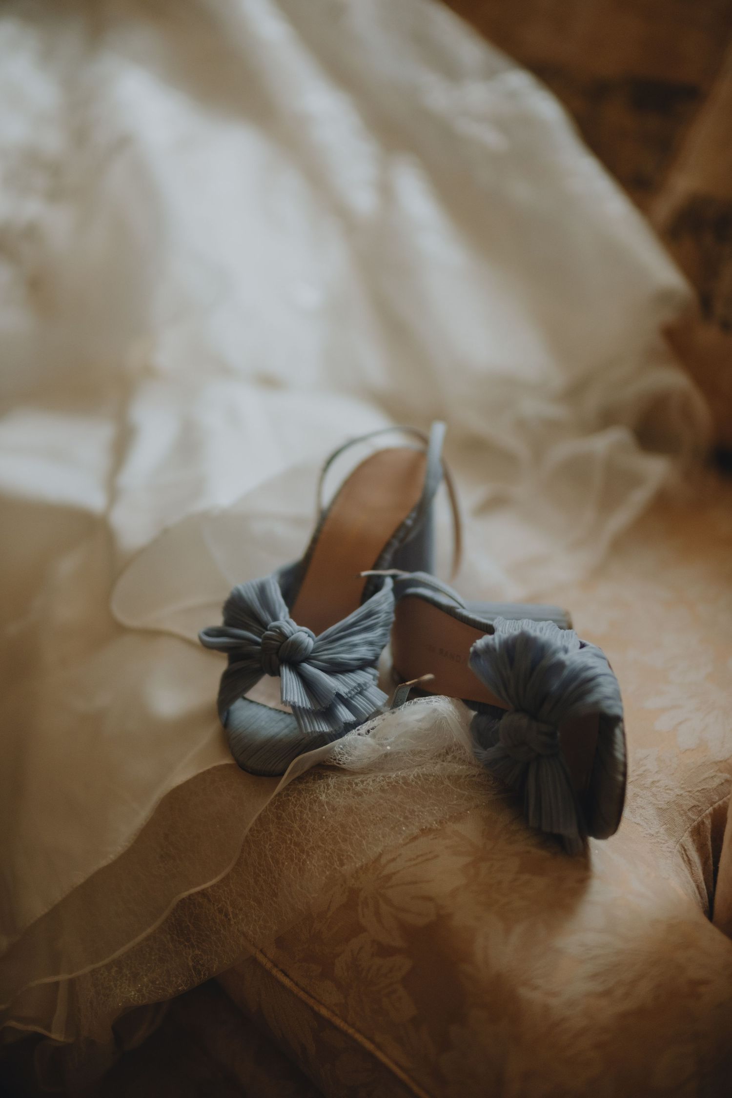 Elegant gray bridal shoes with bow detail resting on white wedding dress fabric.