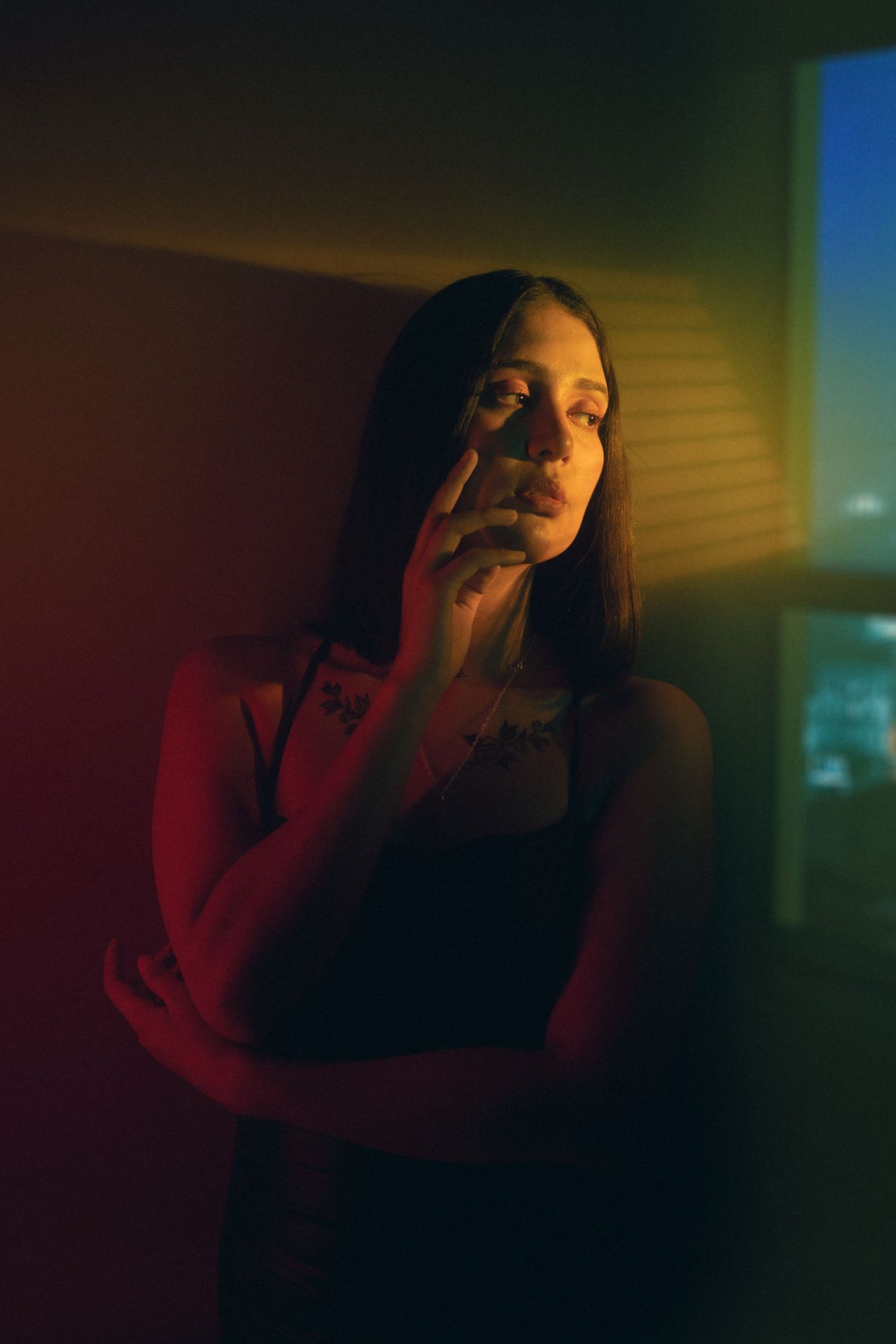 Atmospheric nighttime portrait with dramatic red and blue lighting casting moody shadows on figure in dark room.