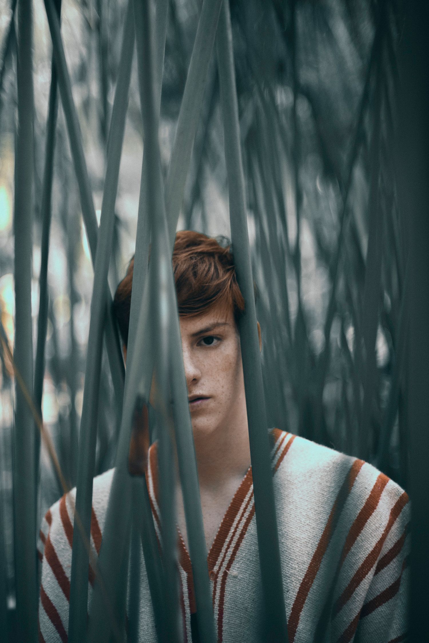 Artistic portrait through bamboo leaves creating dramatic shadows and patterns.