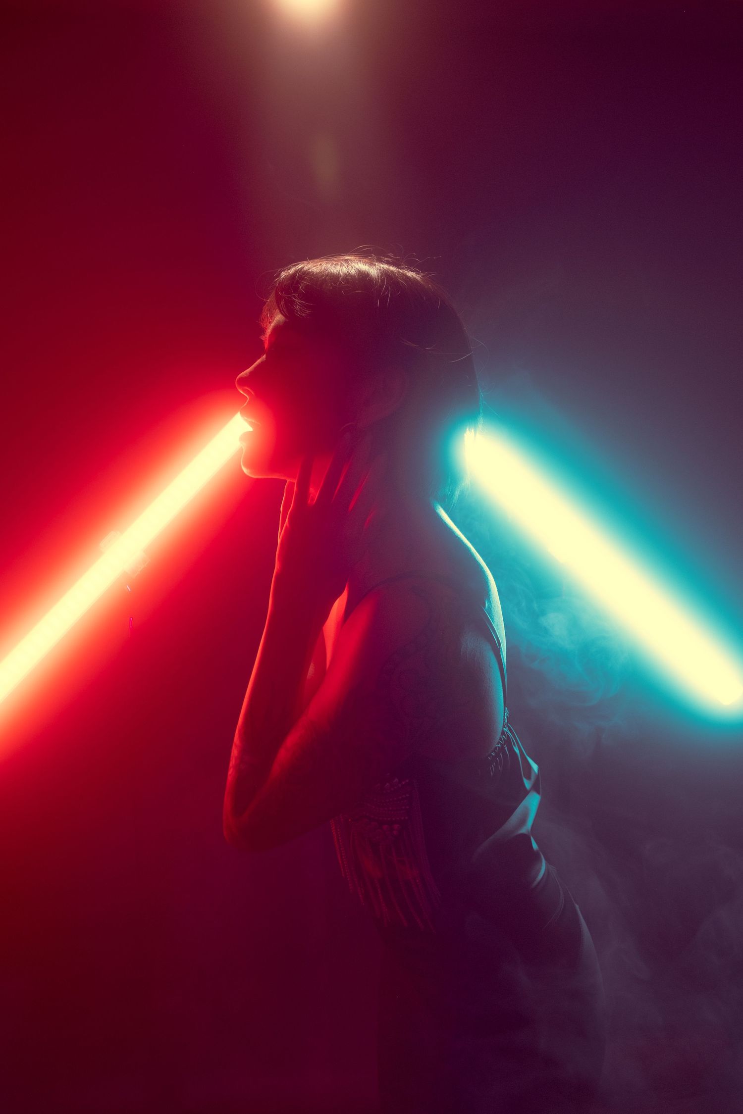 Silhouette between glowing red and blue light beams in smoky dark environment.