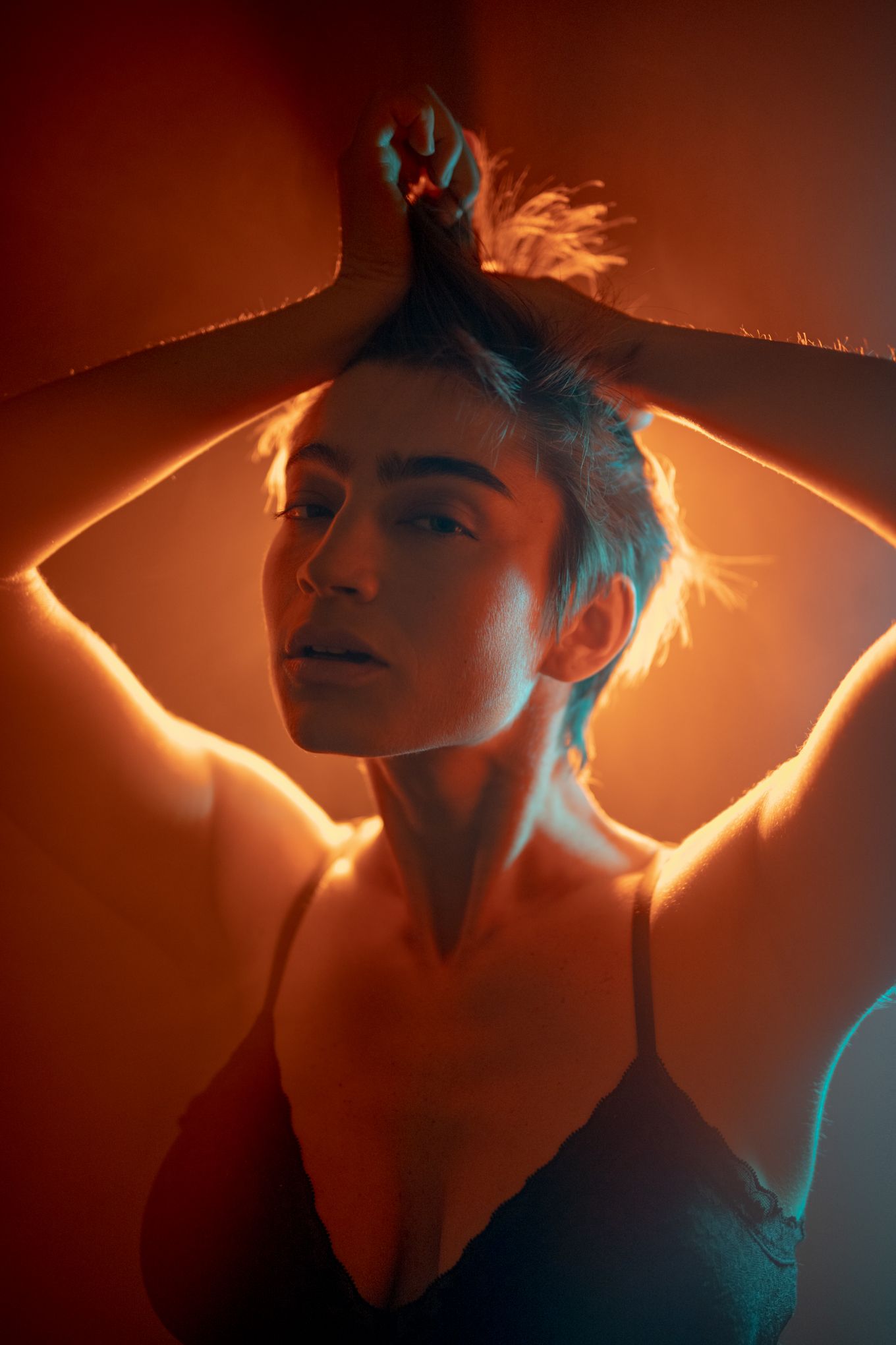 Dramatic backlit portrait with neon glow and raised arms creating geometric shapes.