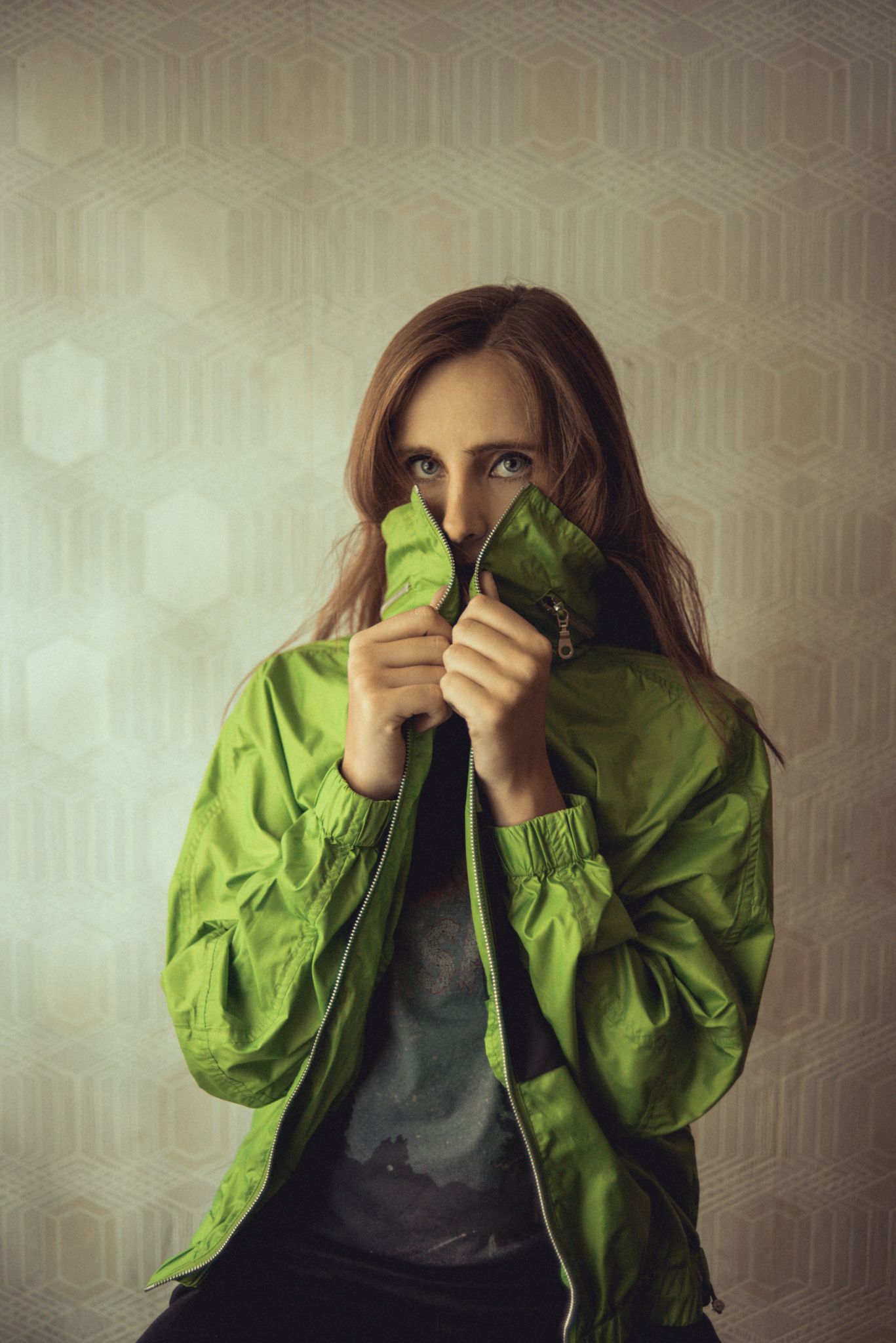 Person in bright green bomber jacket poses against geometric wallpaper.