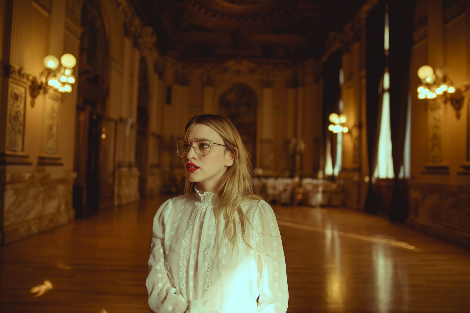 Moody portrait in ornate hallway with vintage lighting and elegant architecture.