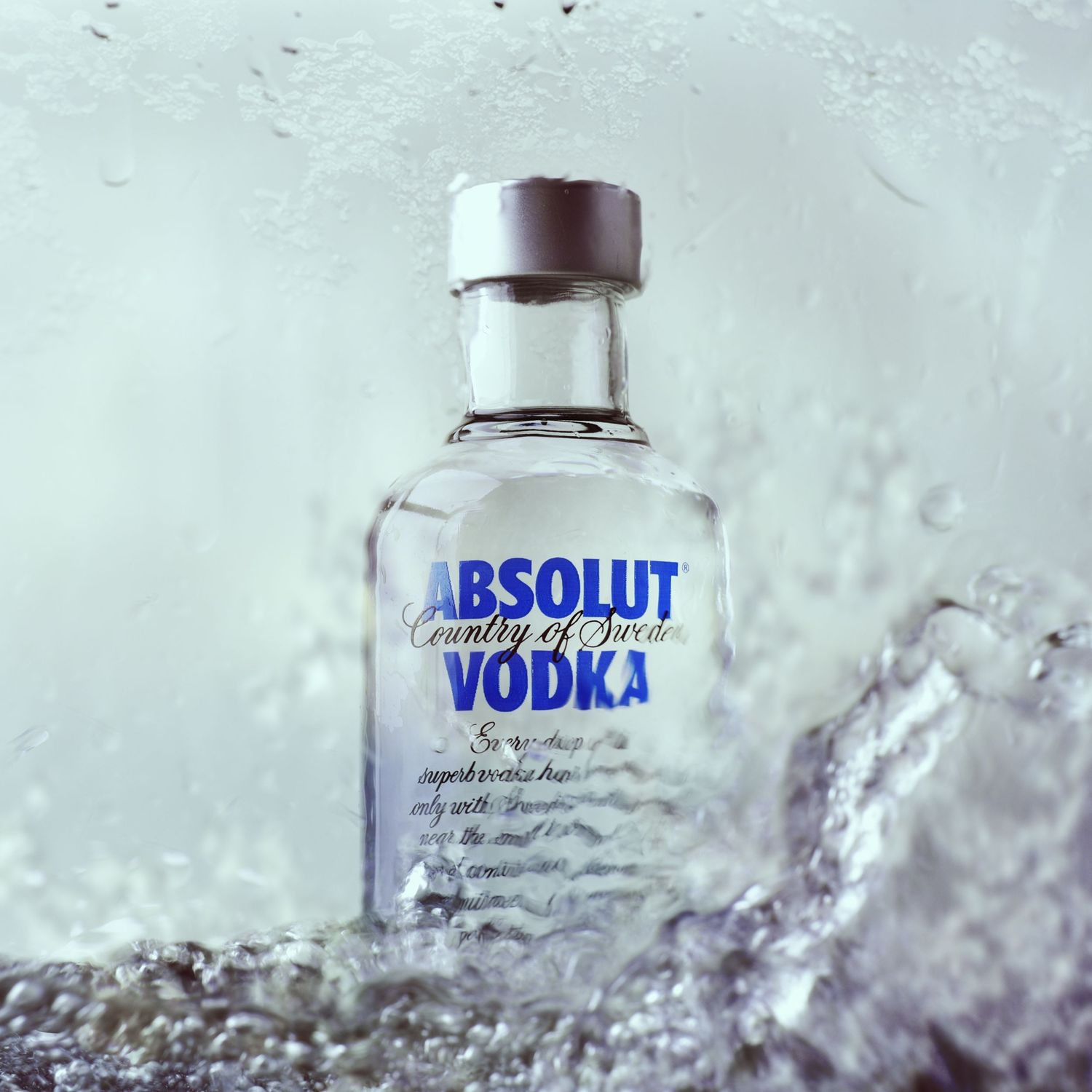 Glass bottles of Absolut vodka with water droplets and condensation on a light background against blurred reflections.