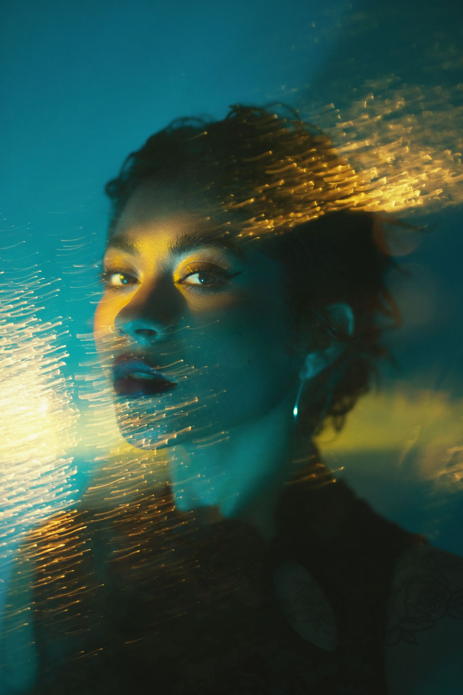 Abstract portrait with golden light effects against turquoise background.