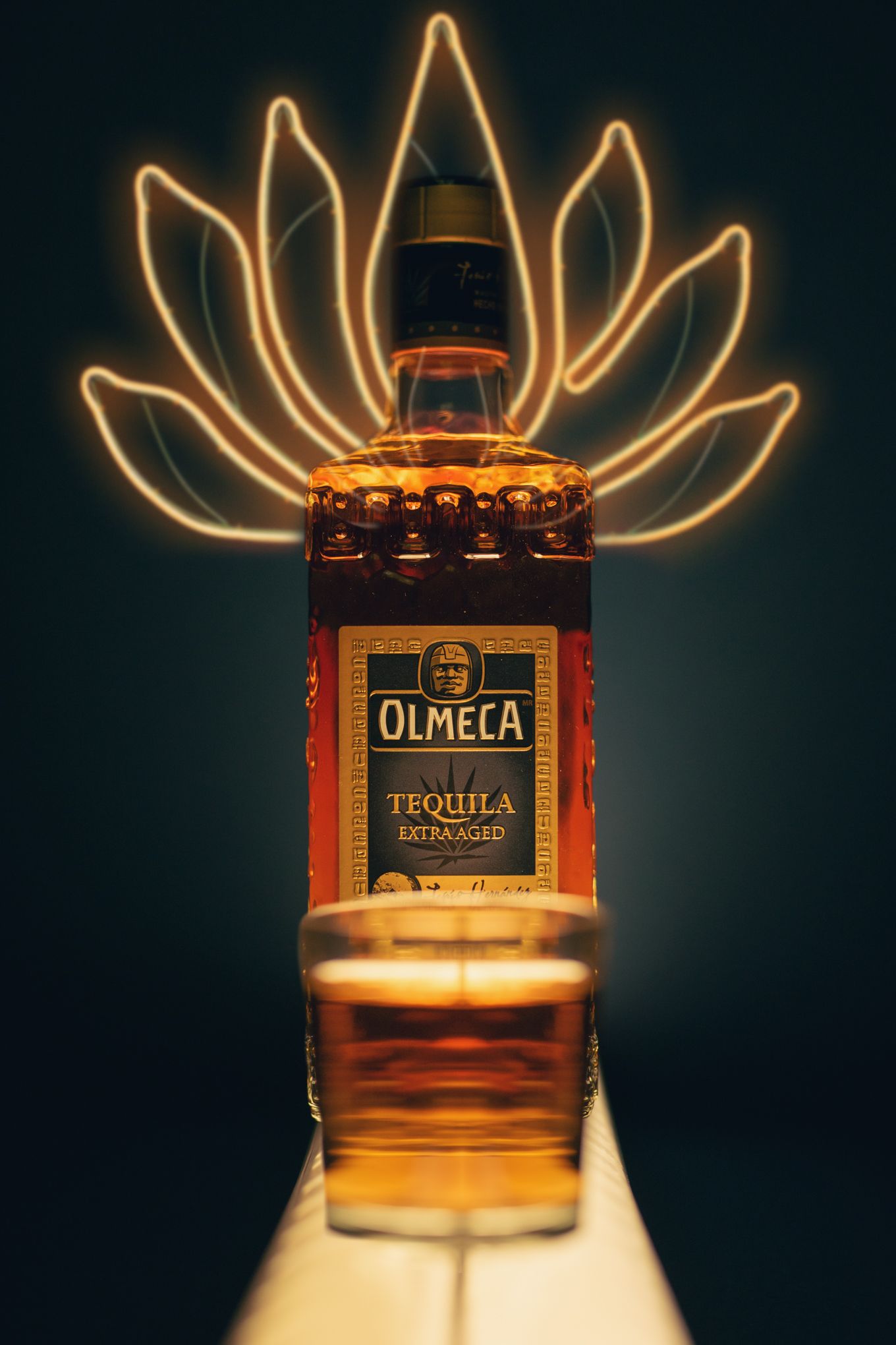 Olmeca tequila bottle illuminated by neon lotus flower light art behind it.