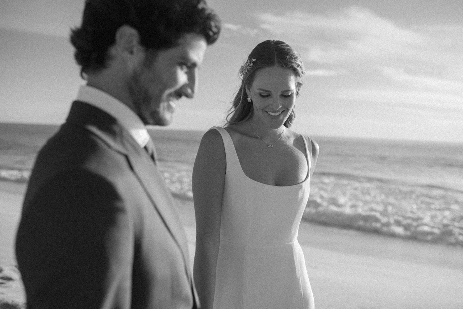 A romantic black and white beach wedding portrait with ocean waves in the background.