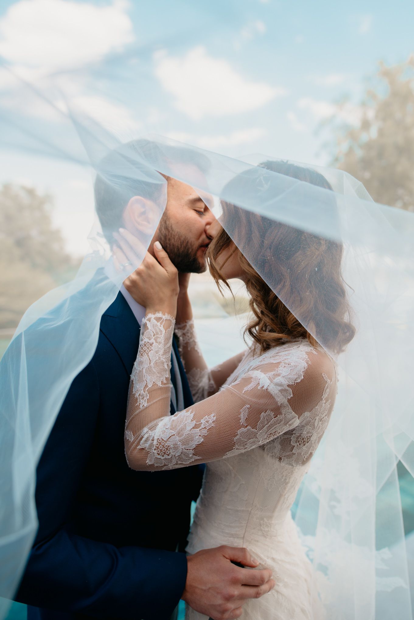 Romantic mountain wedding portrait with couple kissing under flowing veil.