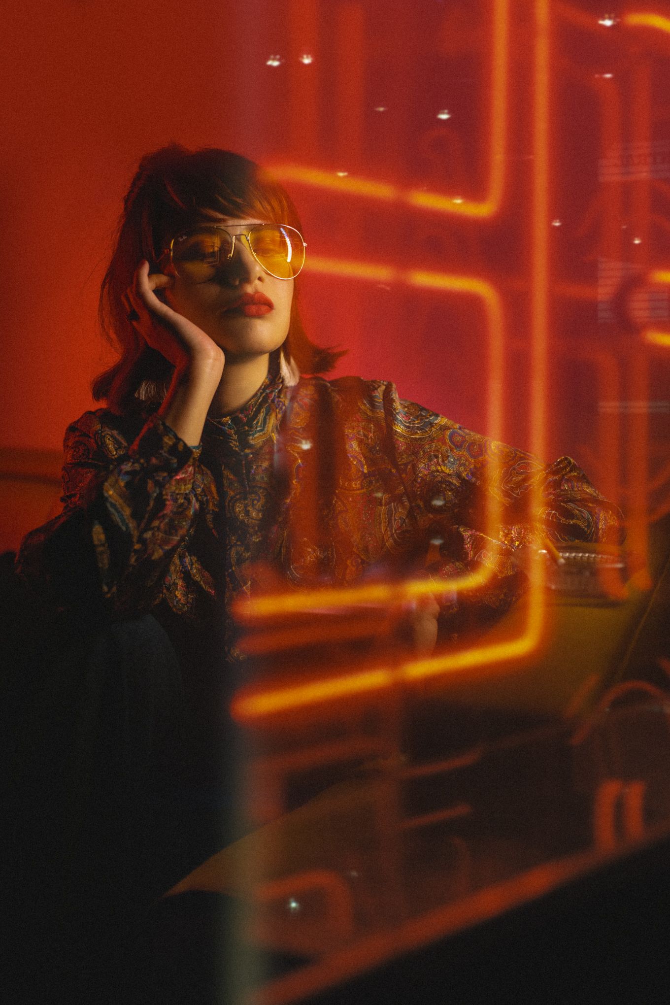 Retro-styled portrait with orange neon lighting and vintage sunglasses in dark setting.