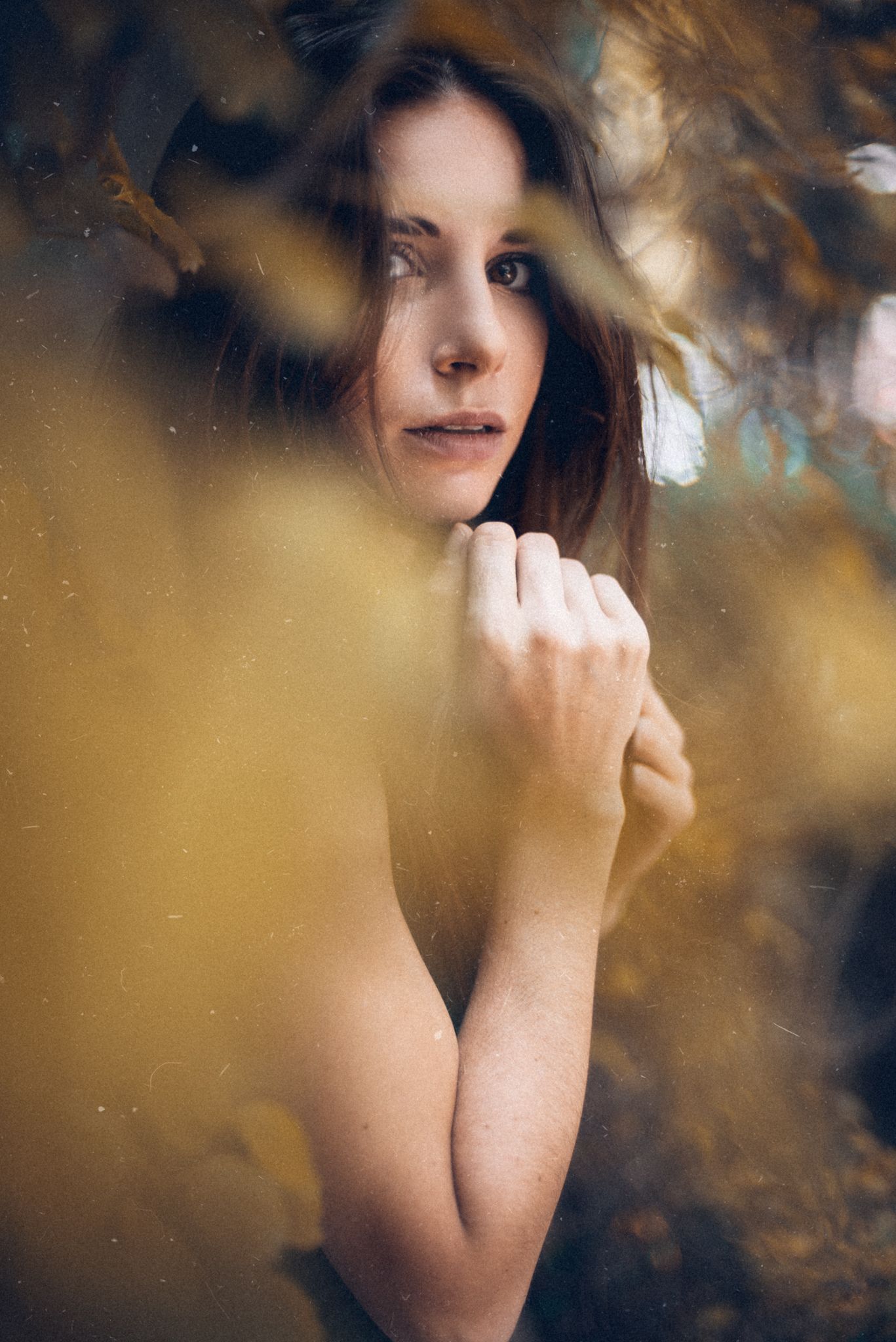Artistic portrait through golden bokeh and fall foliage.