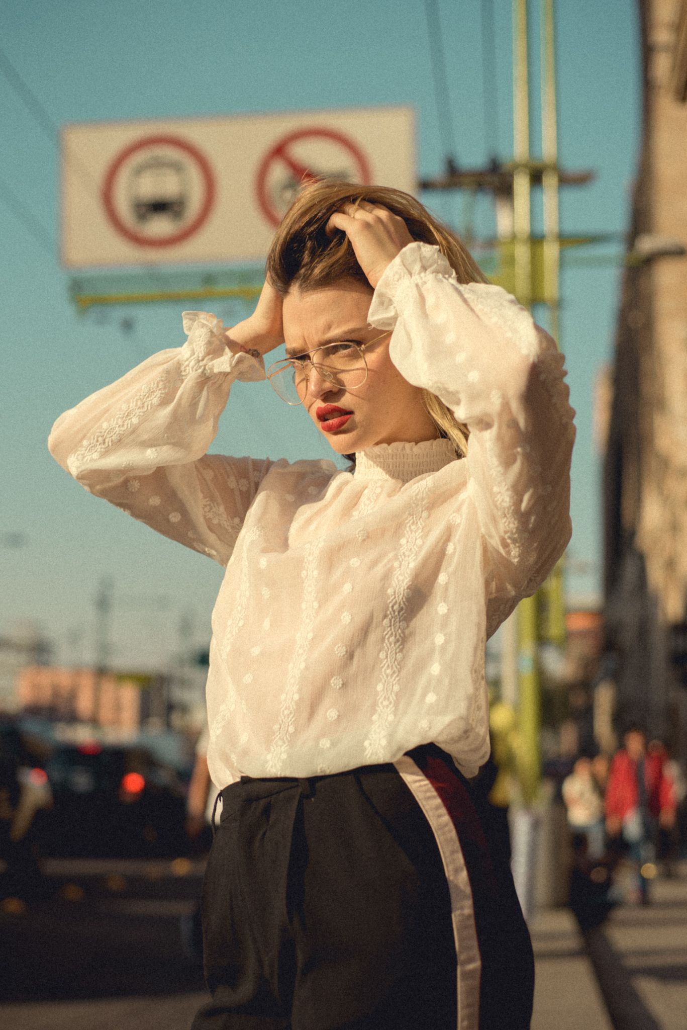 Street fashion portrait with vintage white blouse against urban backdrop and traffic signs.