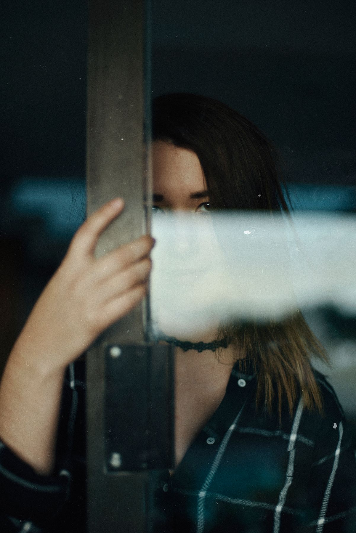 Artistic photo of person partially hidden behind frosted glass with moody lighting.
