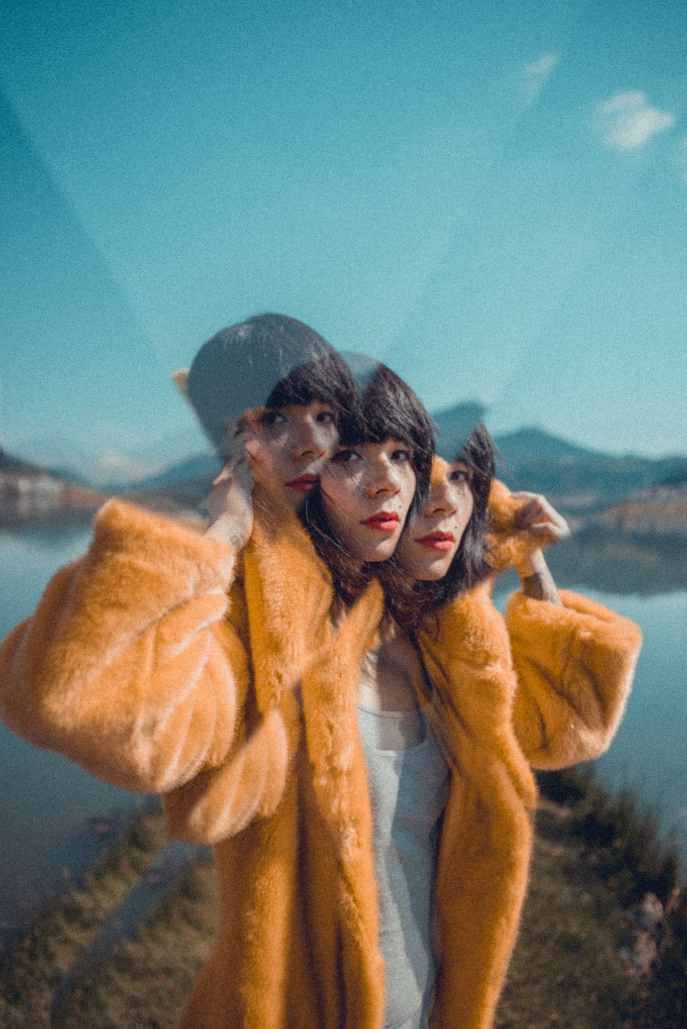 Double exposure portrait in yellow fuzzy coat against mountain landscape.