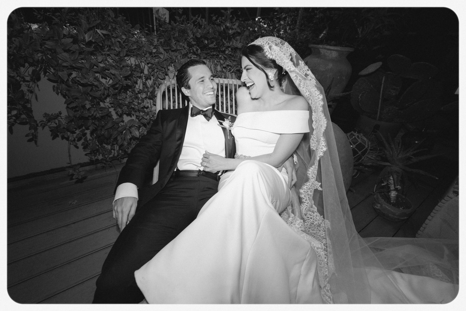 A vintage black and white wedding photograph showing a couple sitting together, with the bride wearing a traditional white gown and veil.
