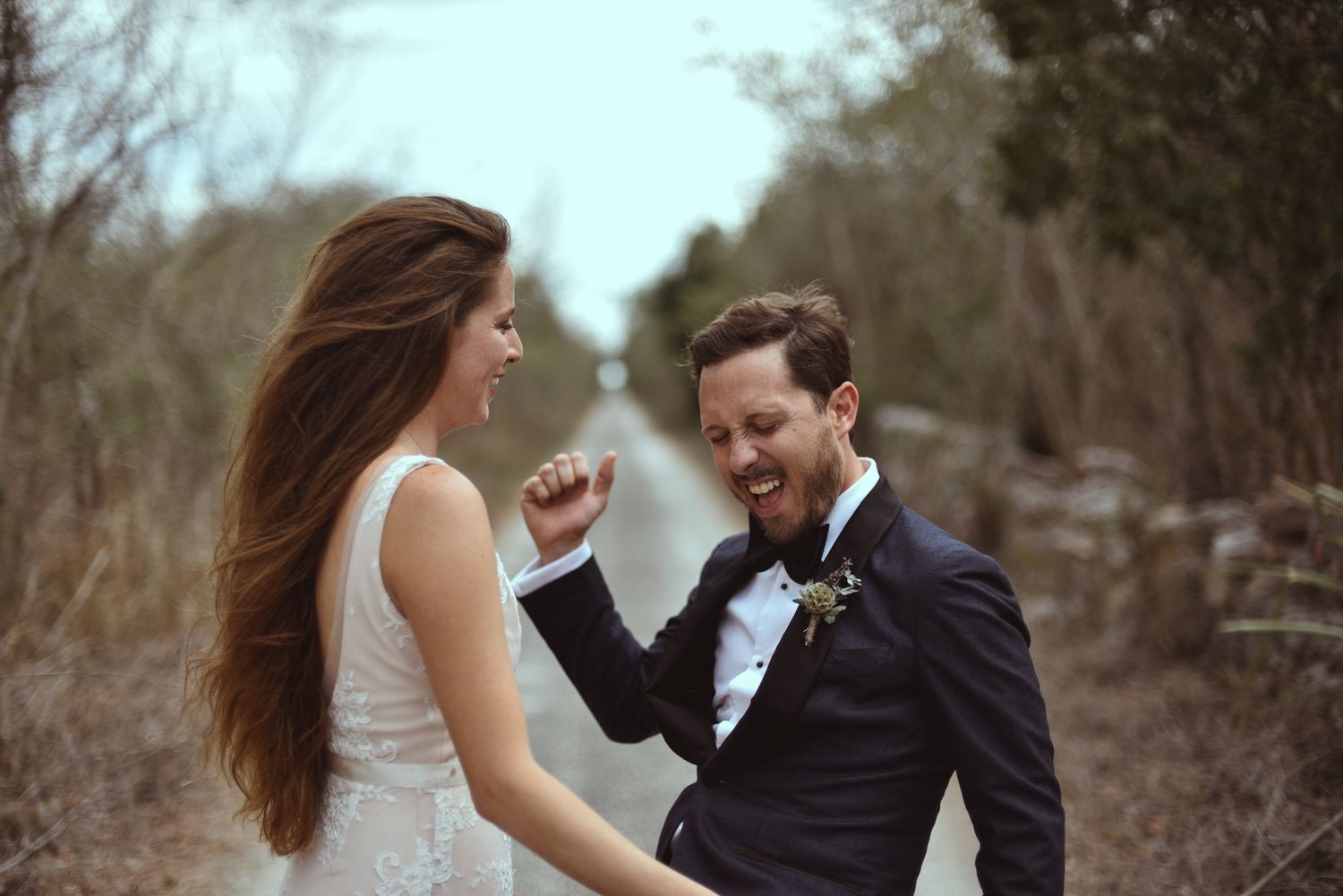 A couple in wedding attire share a joyful moment together on a rustic path during their countryside celebration.