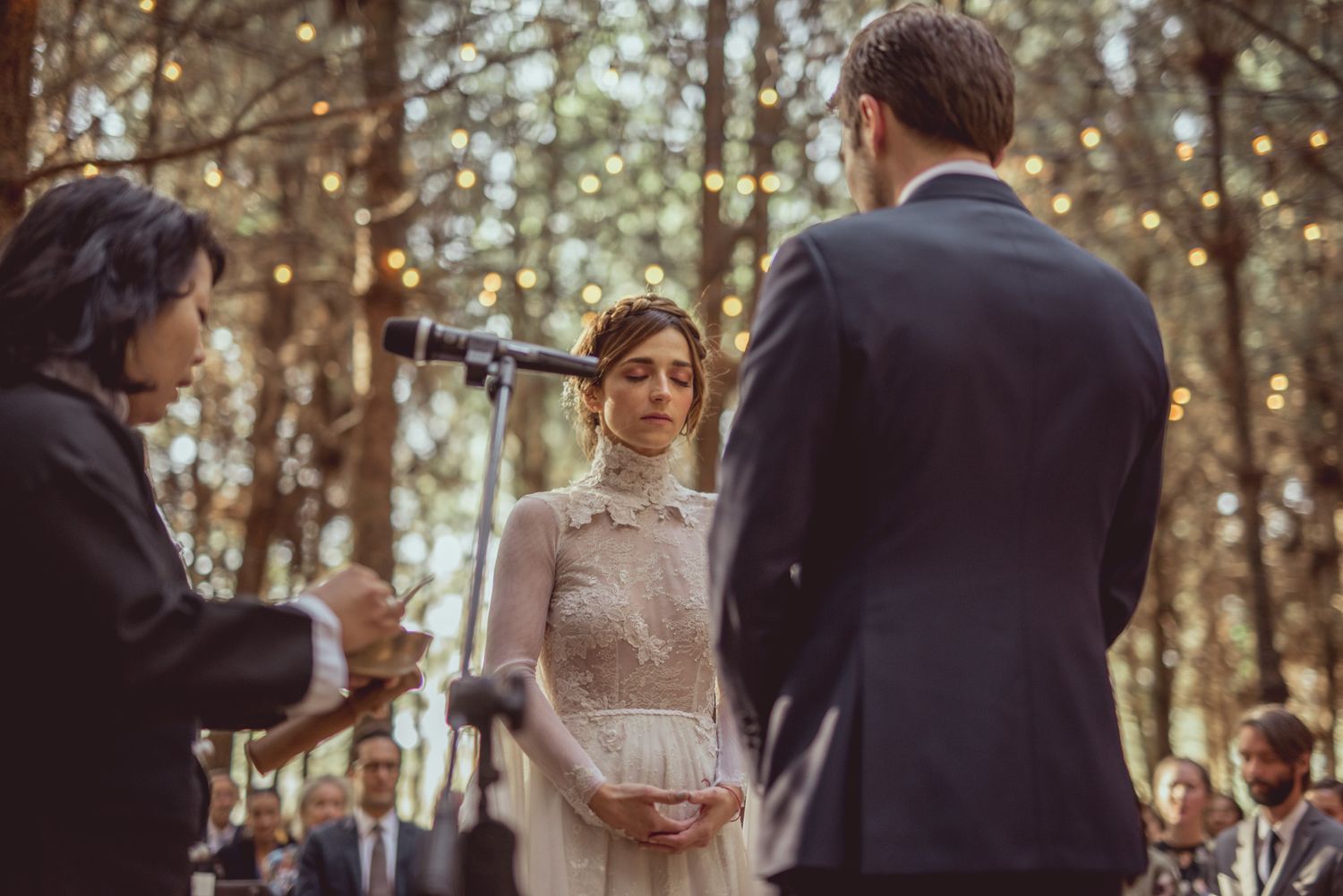 Outdoor forest wedding ceremony with twinkling lights and natural decor during intimate exchange of vows.
