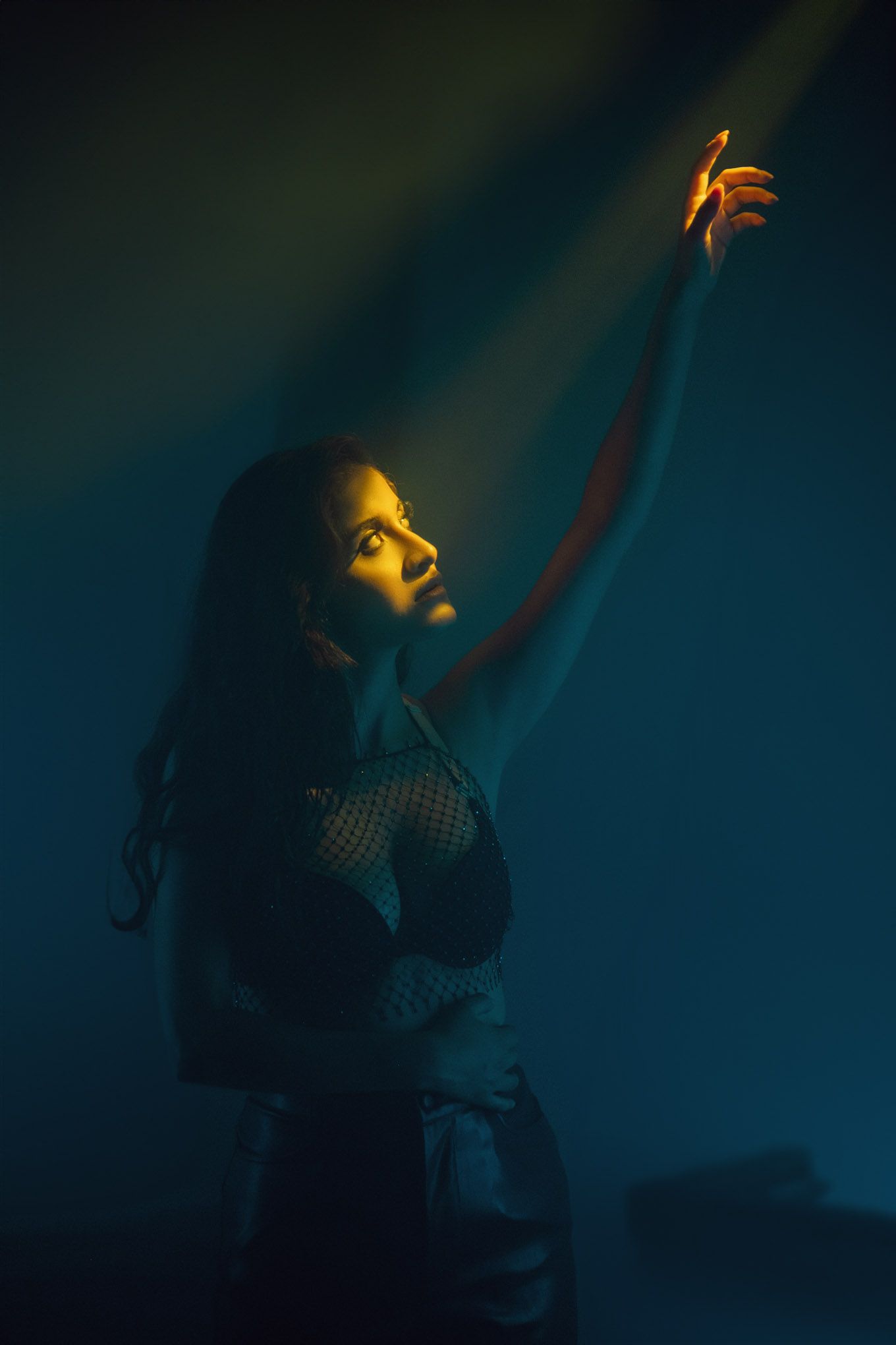 Dramatic silhouette reaching up toward light beam against dark blue background.