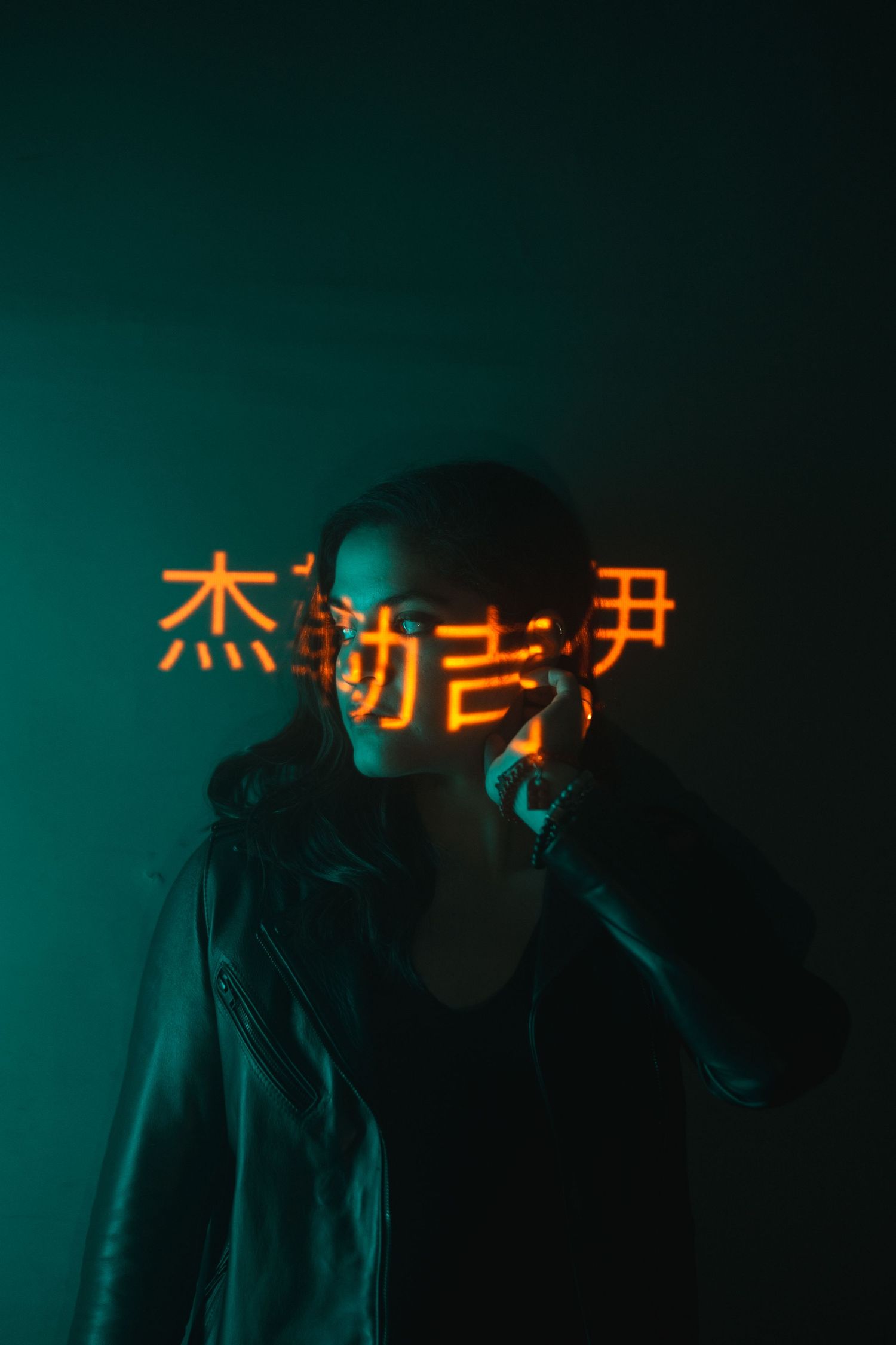 Silhouetted figure in front of neon Chinese characters glowing against dark teal background with moody lighting.
