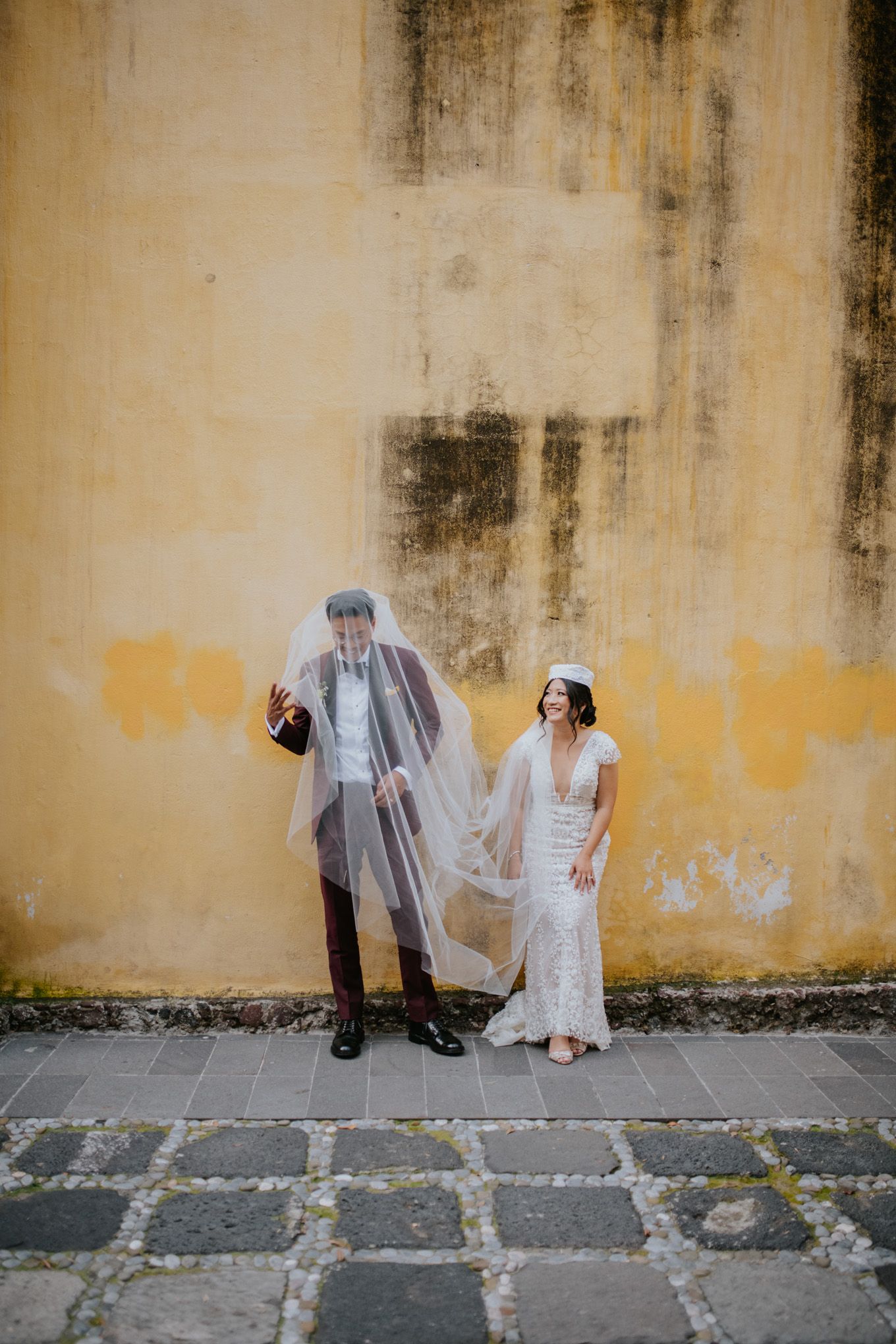Playful wedding portrait against yellow wall with couple showing personality.