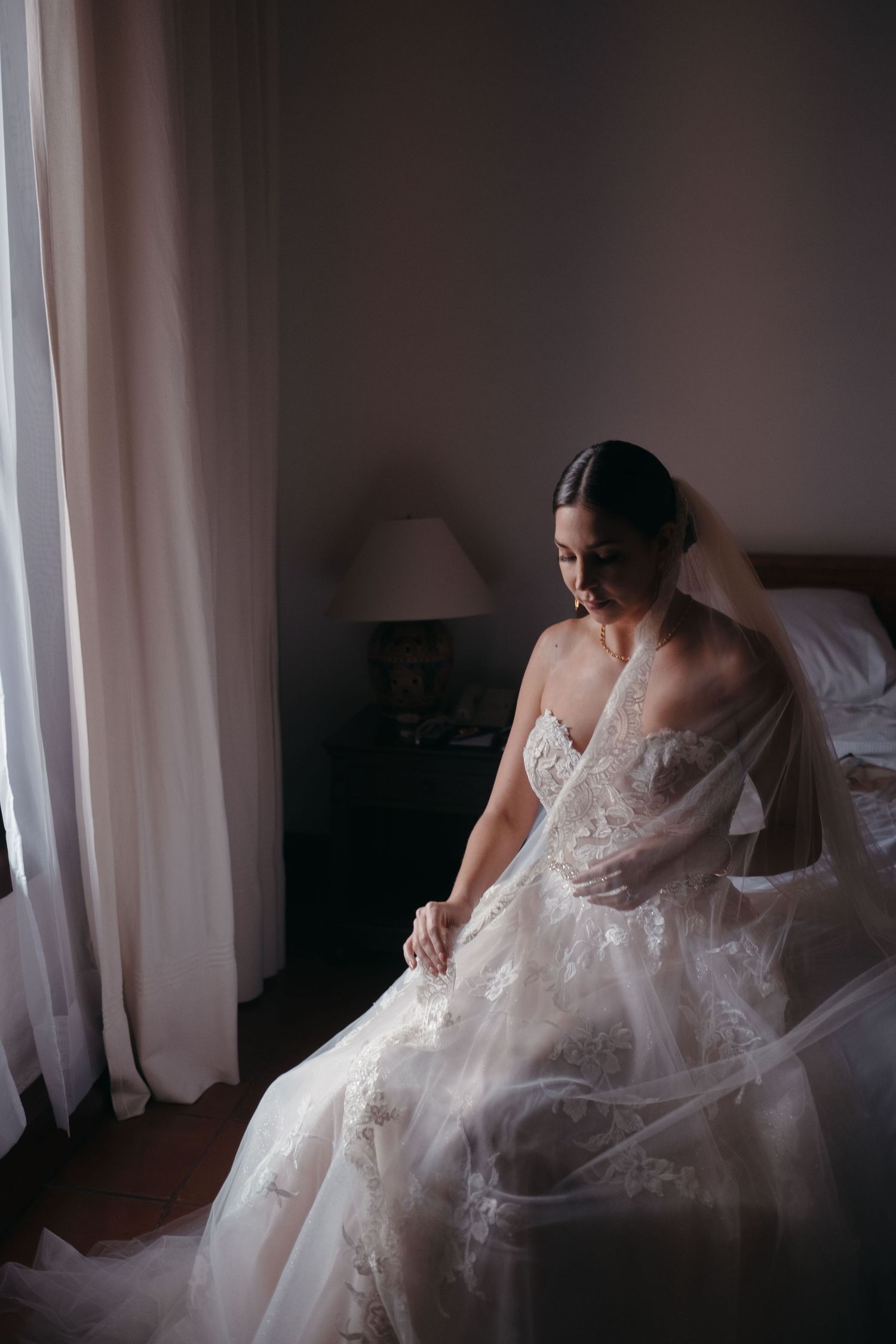 A bridal portrait by a window featuring an elegant white lace wedding dress with delicate details.