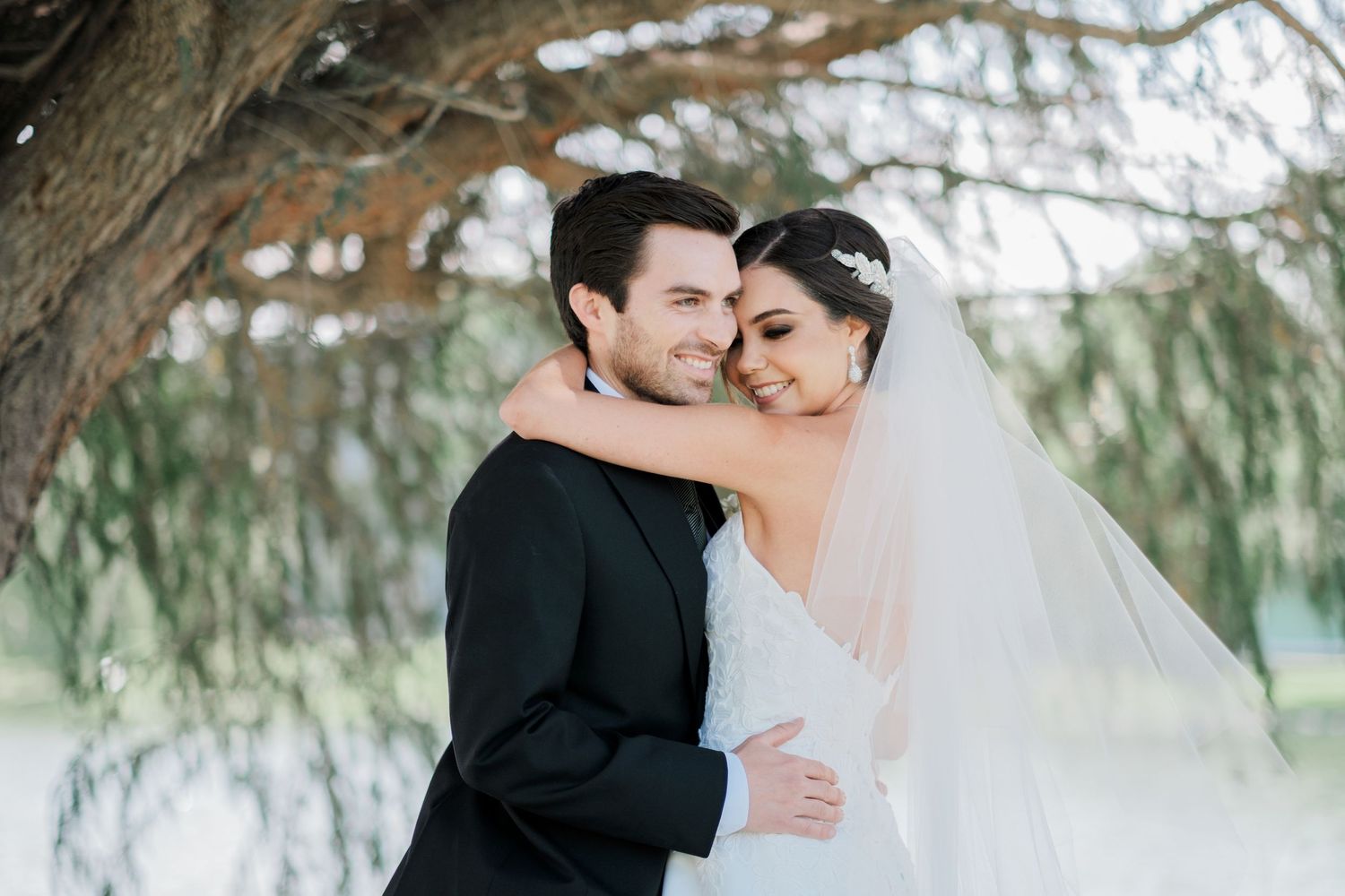 A romantic embrace under willow trees captures a tender wedding moment.