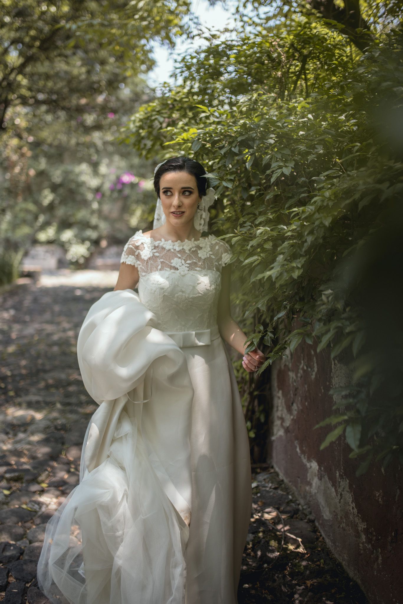 A classic white wedding dress billowing in the breeze along a garden pathway.
