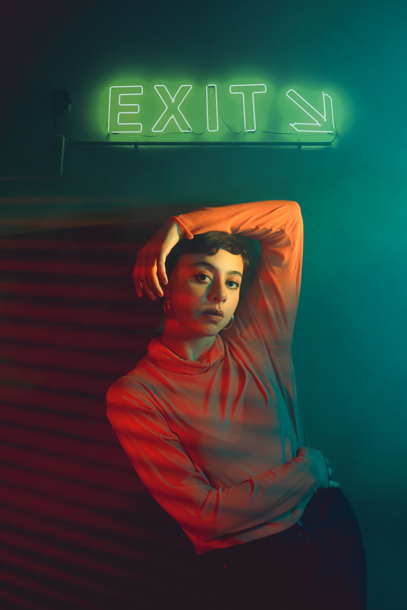 Dramatic portrait under neon exit sign with contrasting red and teal lighting.