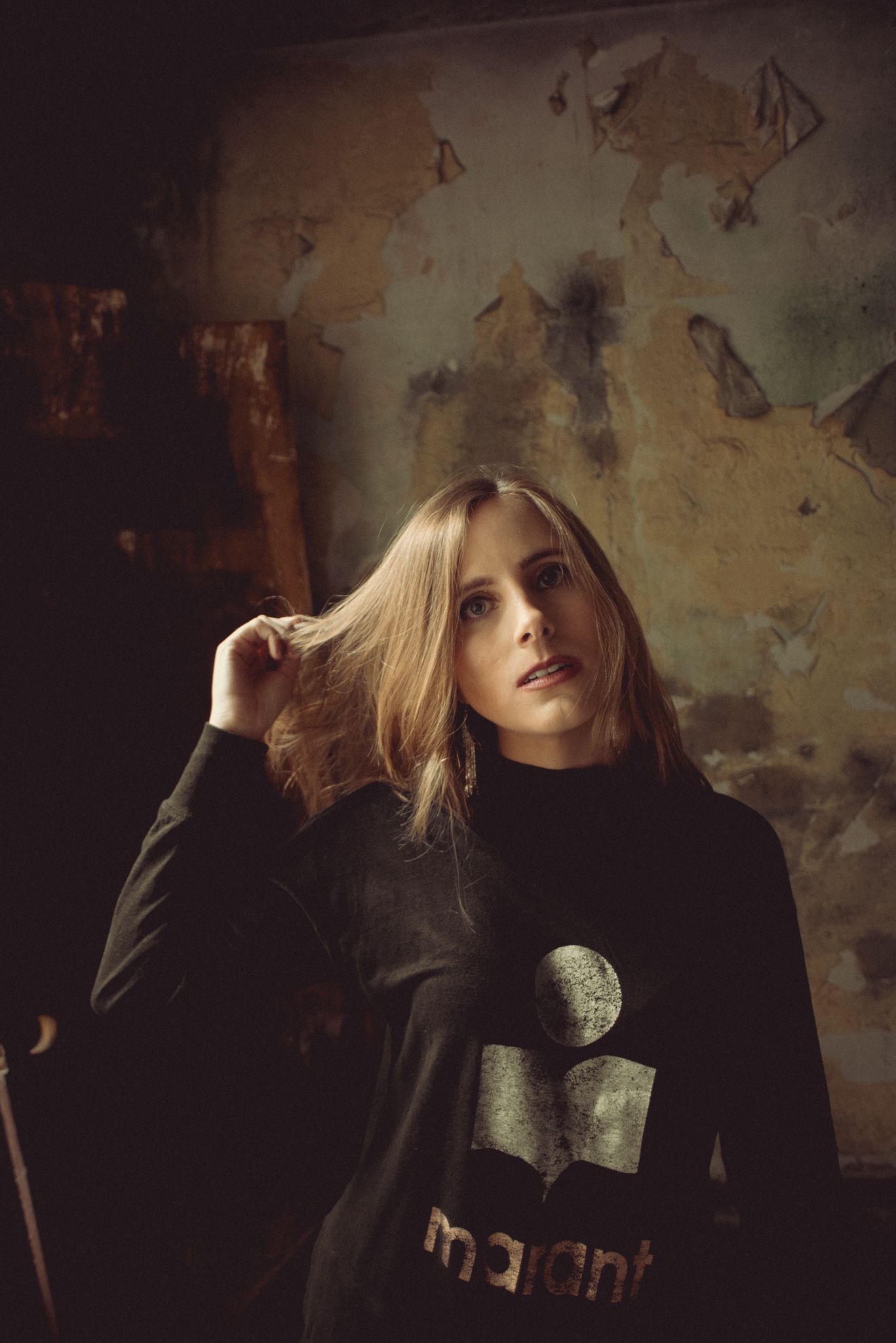 Atmospheric portrait in black sweater against textured wall.