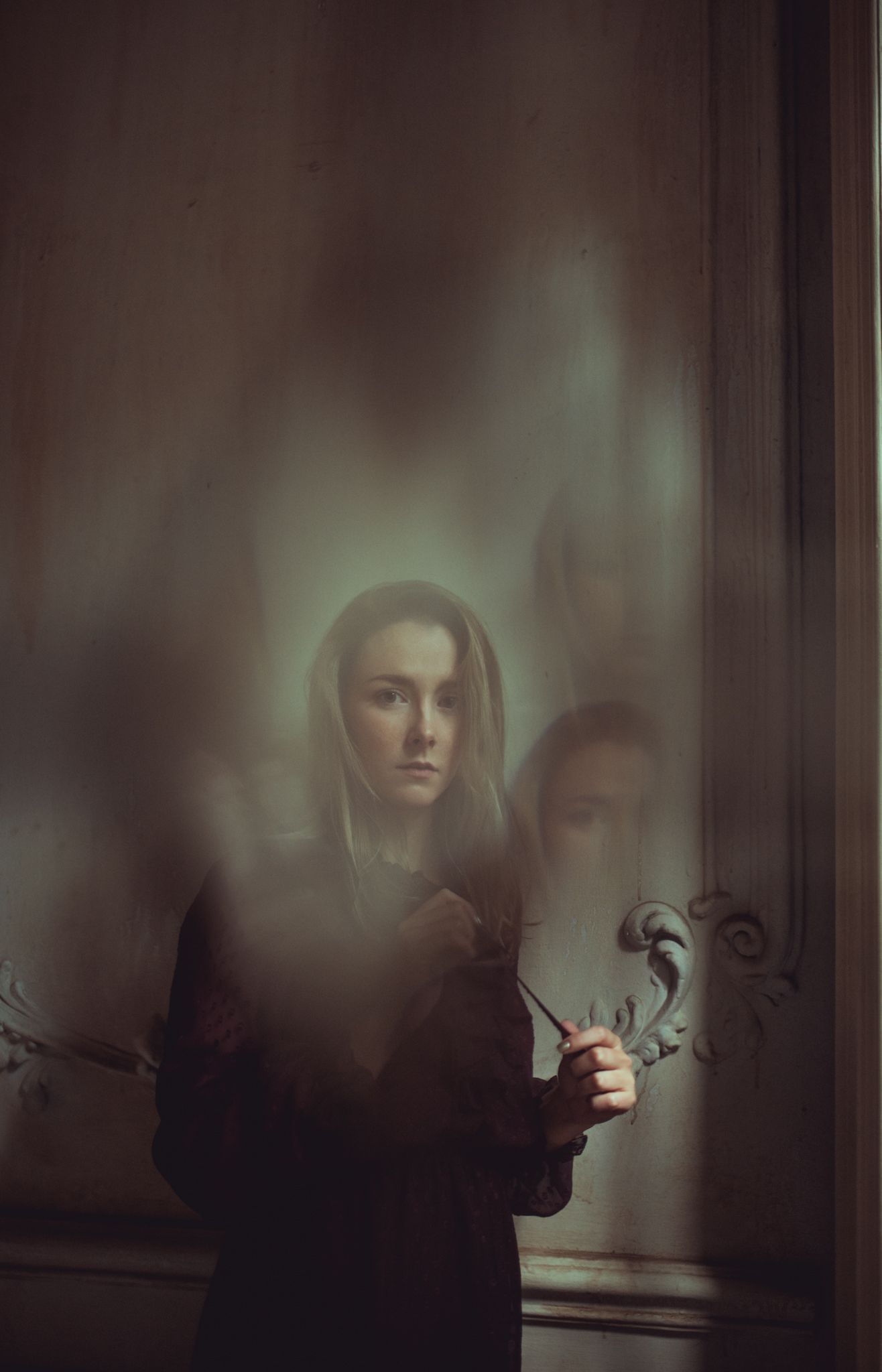 Dark atmospheric portrait with soft focus and ornate wall details.