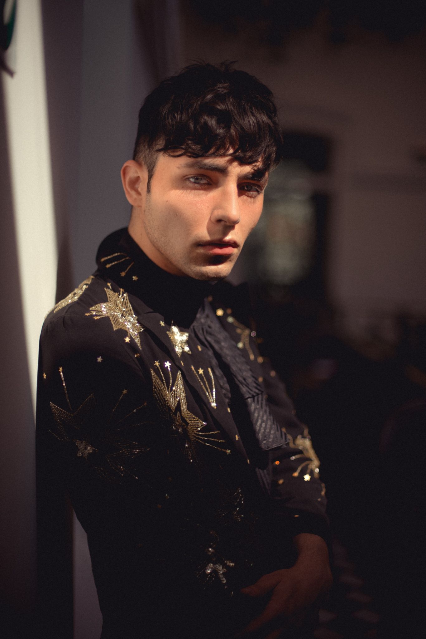 Fashion portrait of model wearing black embellished turtleneck in dramatic lighting.