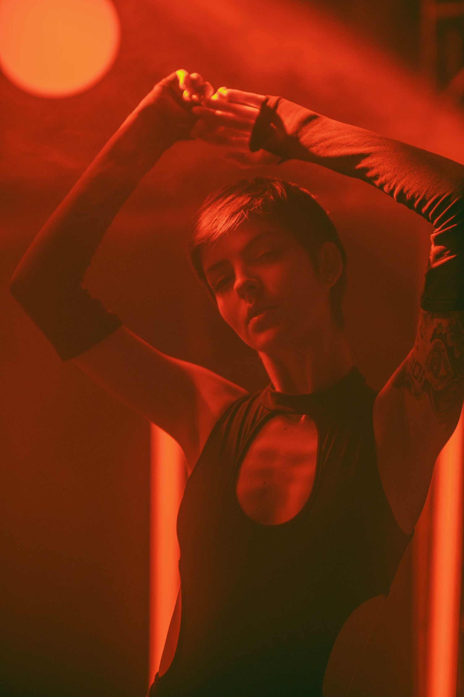 Dramatic portrait in red stage lighting with dancer striking a pose.
