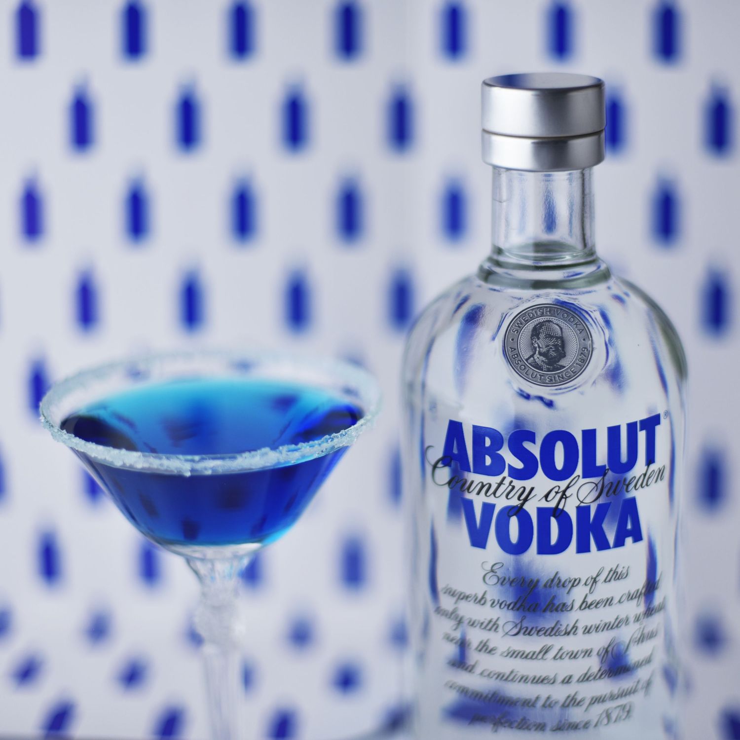 Absolut vodka bottle with blue martini cocktail against patterned blue background.