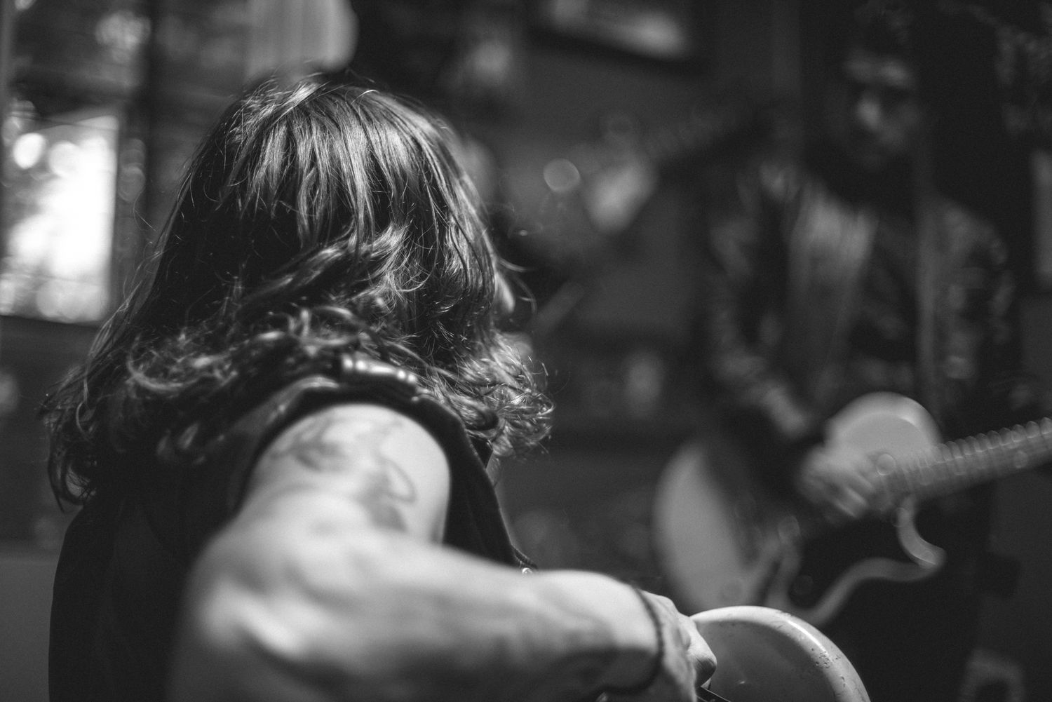 Black and white profile shot of musician with long hair performing on stage.