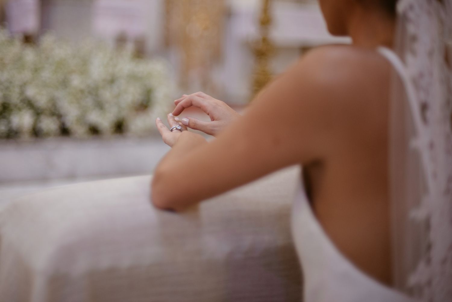 Close-up shot of hands folded in prayer during a wedding ceremony with white decorations.