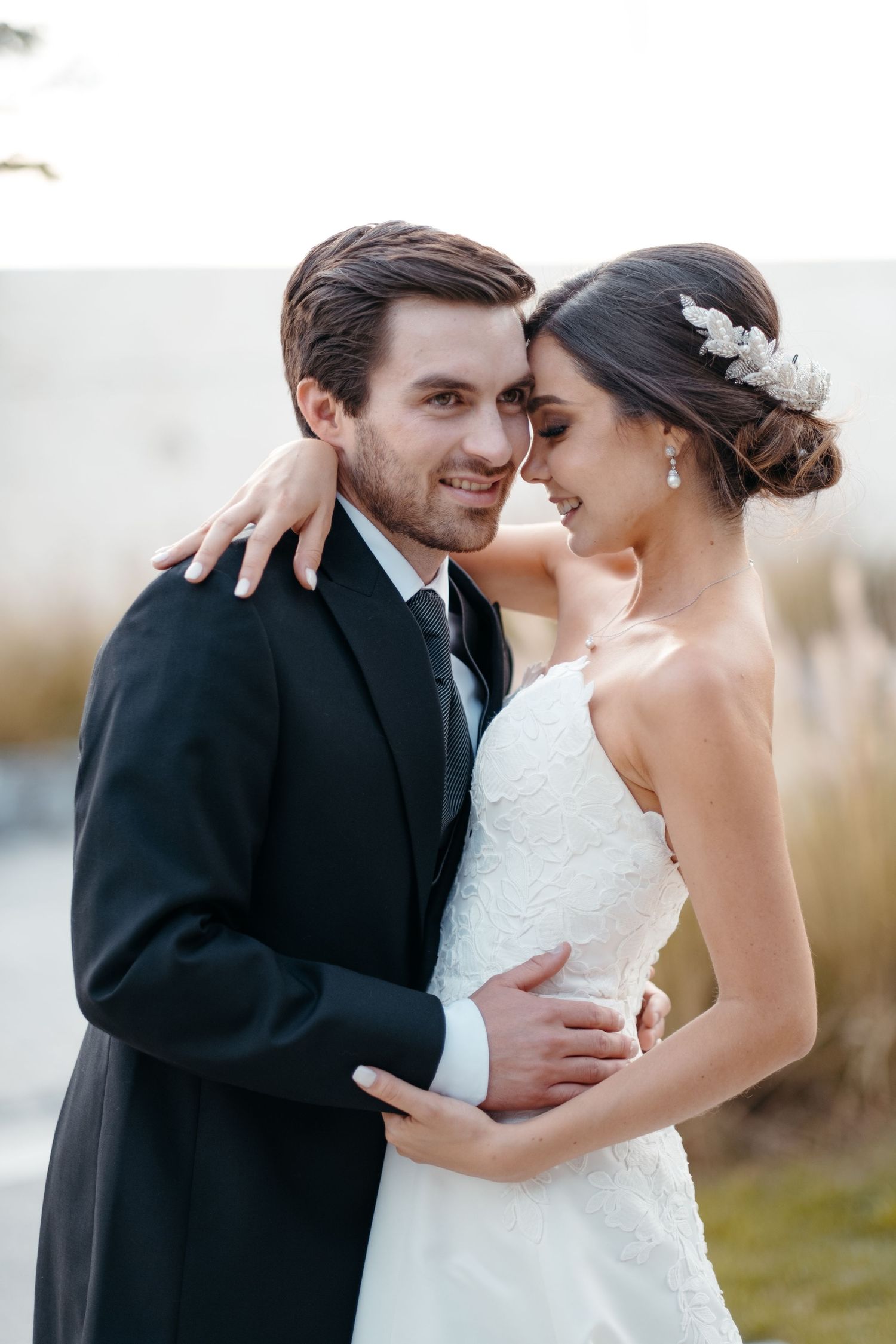 A tender wedding portrait showing a couple in elegant attire embracing outdoors.