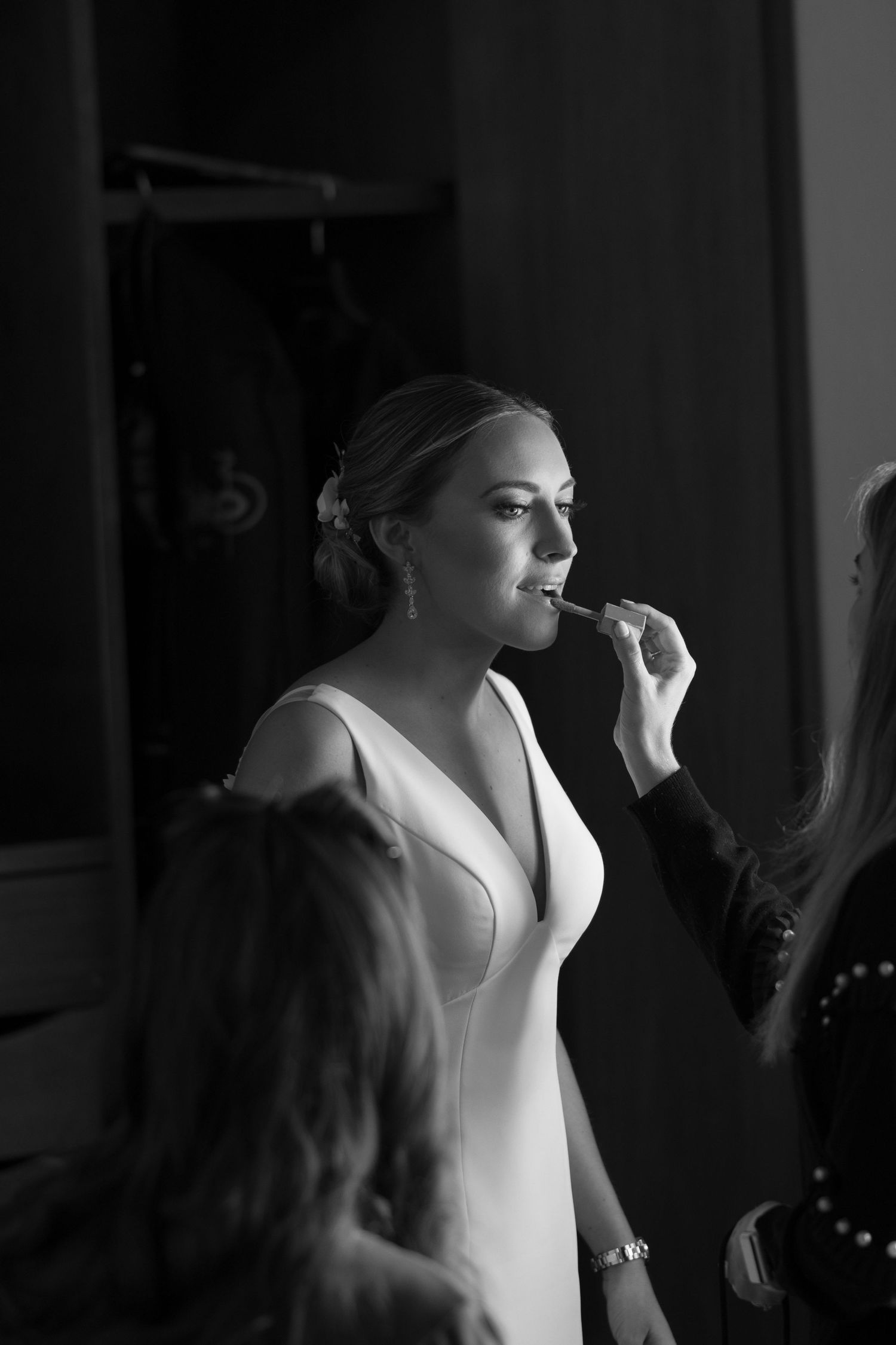 Getting ready before the wedding ceremony wearing an elegant white V-neck dress while having makeup applied.