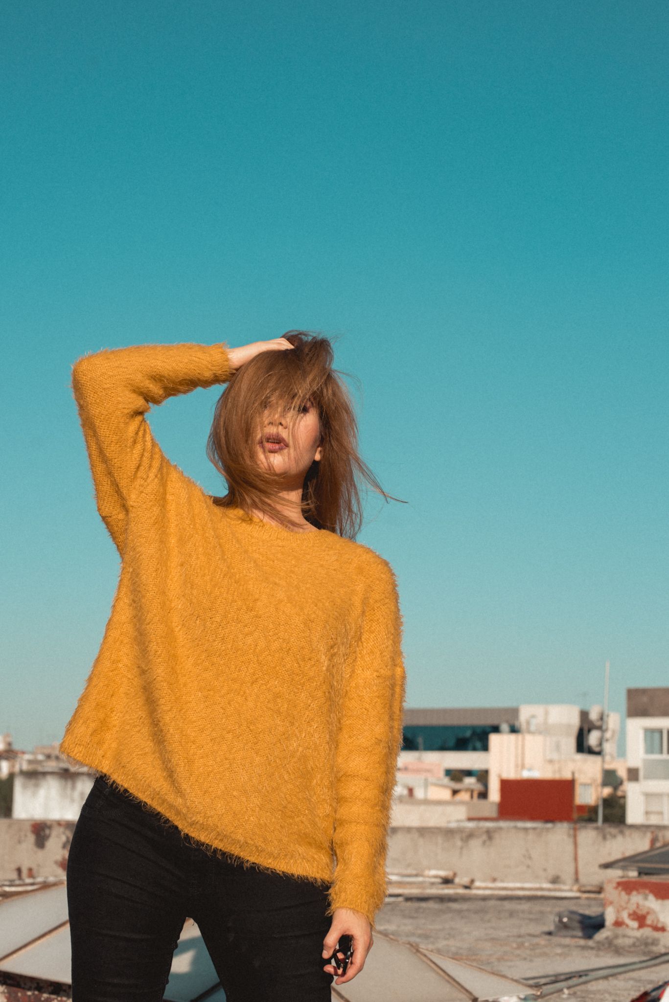 Rooftop fashion portrait in mustard sweater against bright blue sky.