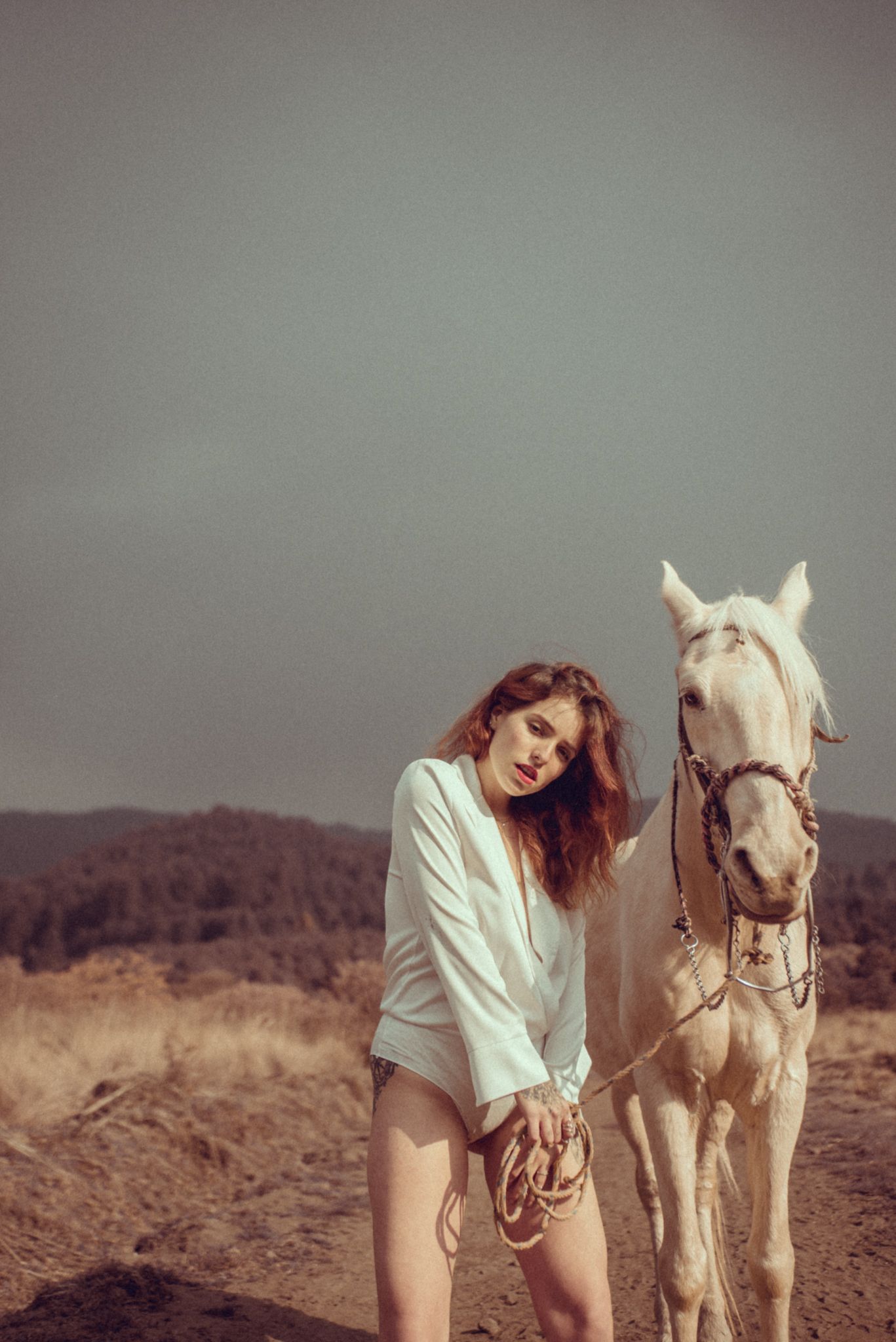 A white horse and person in white outfit pose together against a gray outdoor backdrop.
