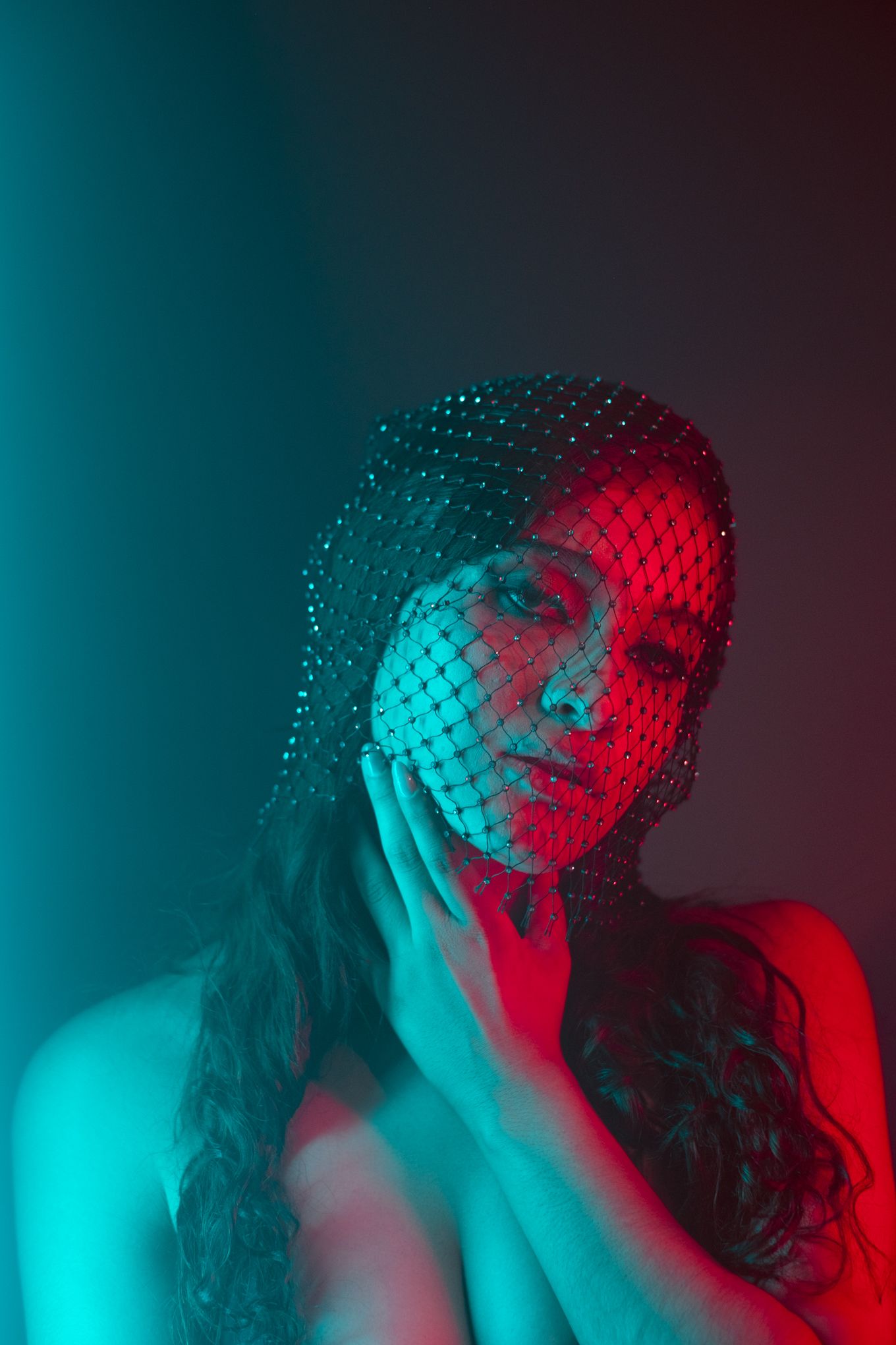 Artistic portrait with dramatic red and teal lighting creating a moody atmosphere through mesh netting overlay.
