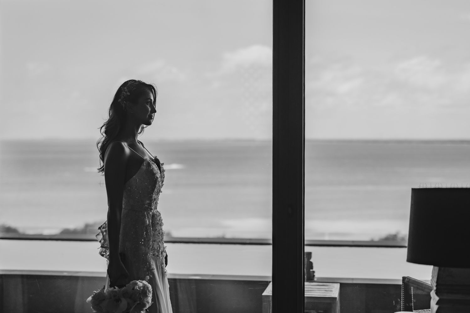 Black and white photo of a silhouetted figure standing on an oceanfront balcony against a bright horizon.