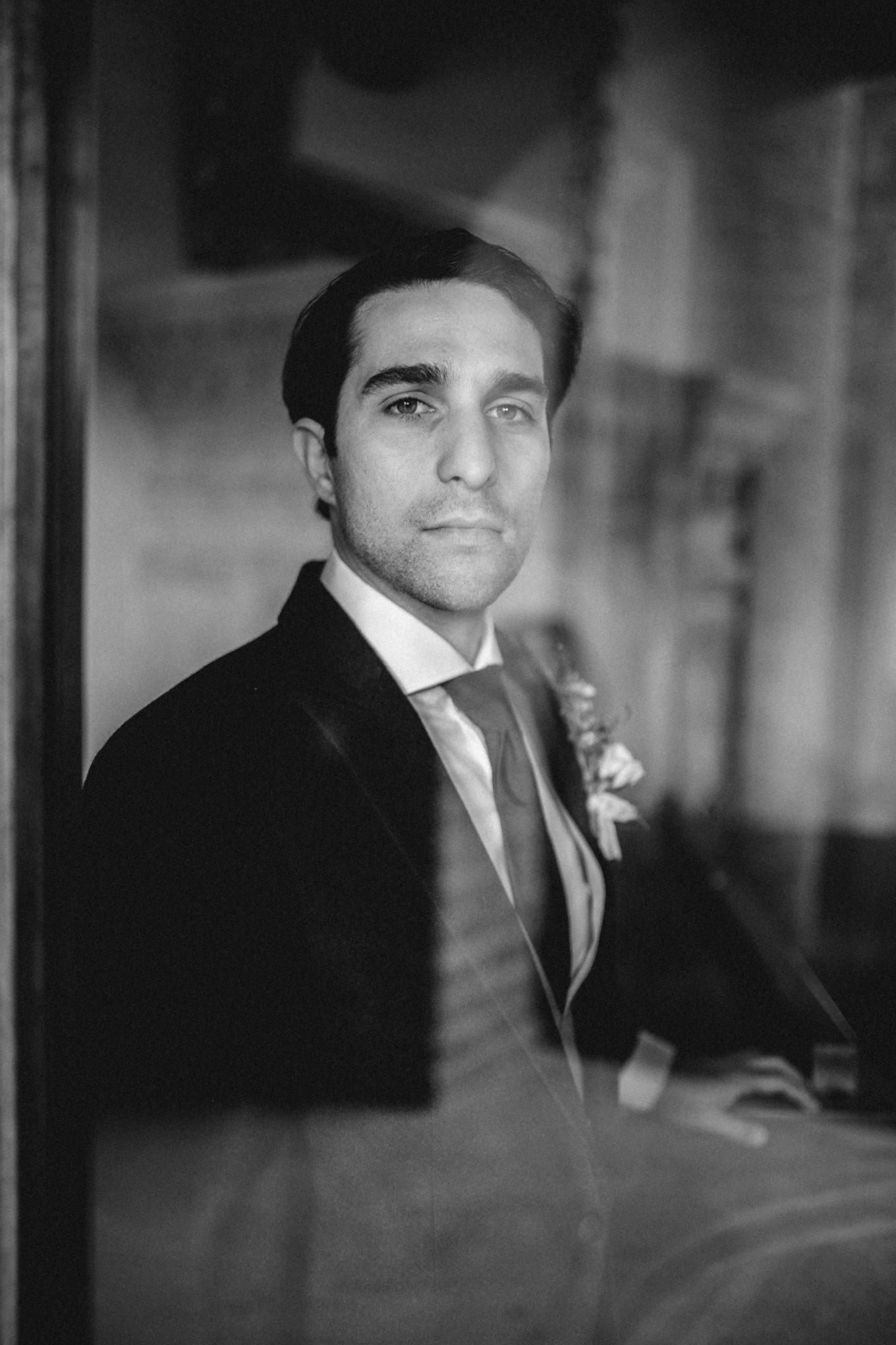 Black and white portrait photograph of a groom wearing a dark suit with boutonniere at a wedding.