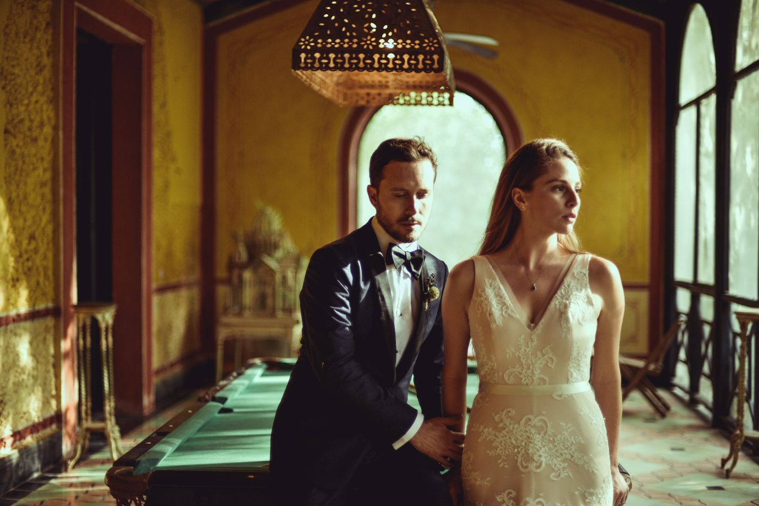 A couple stands together in an elegant dressed up corridor with warm lighting from vintage chandeliers.