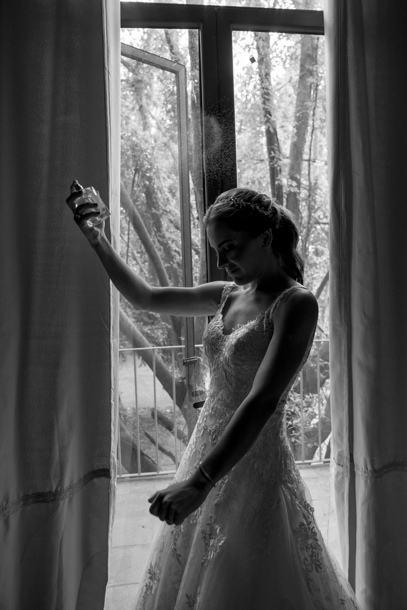 Artistic black and white photograph of a silhouetted figure in a wedding dress standing gracefully by a window.