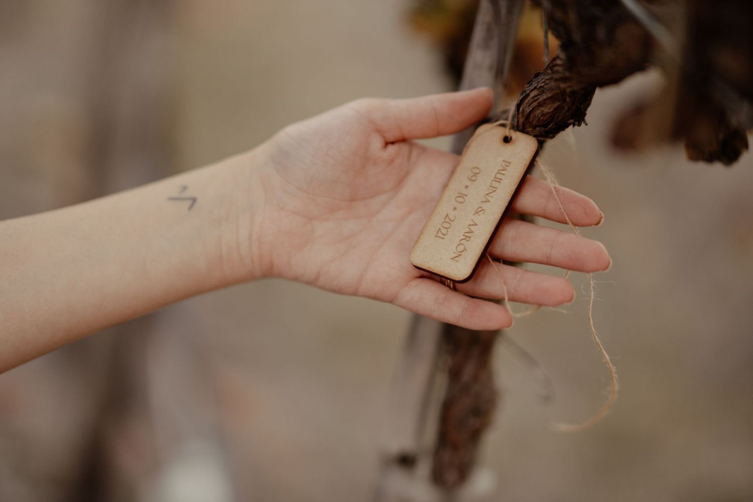 Hand holding a wooden tag with natural string attached.